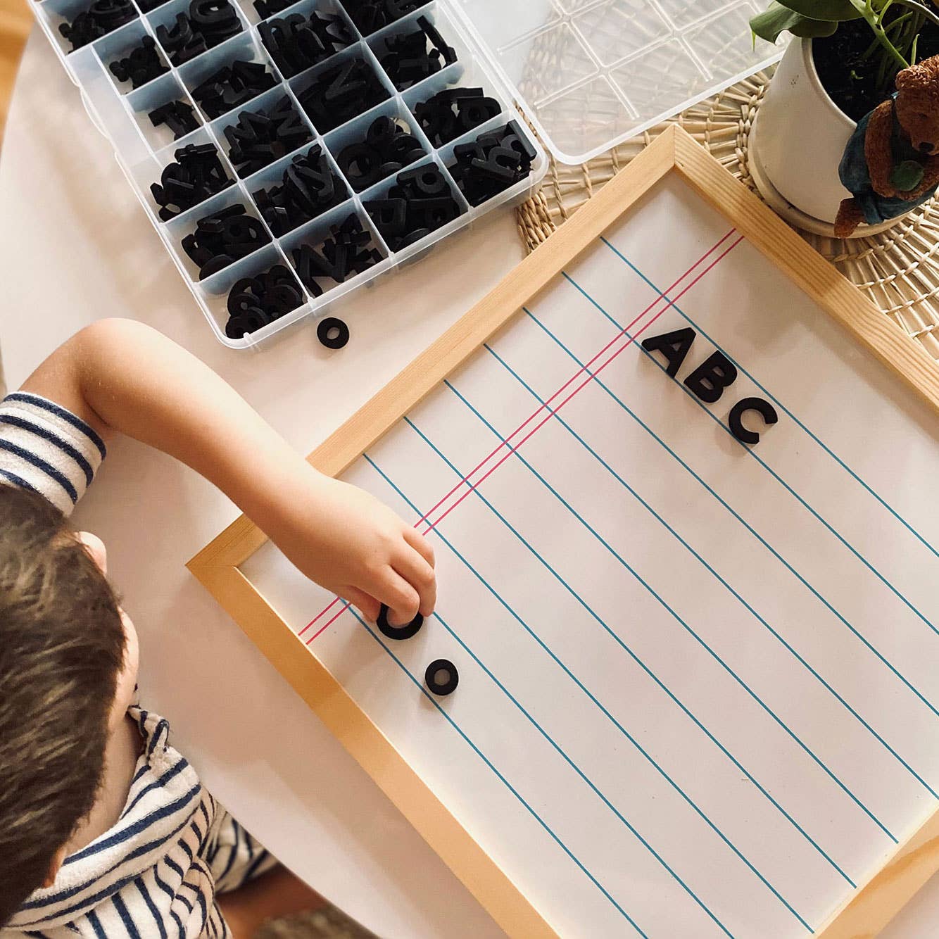 Child playing with black letter beads on a paper with 'ABC' letters