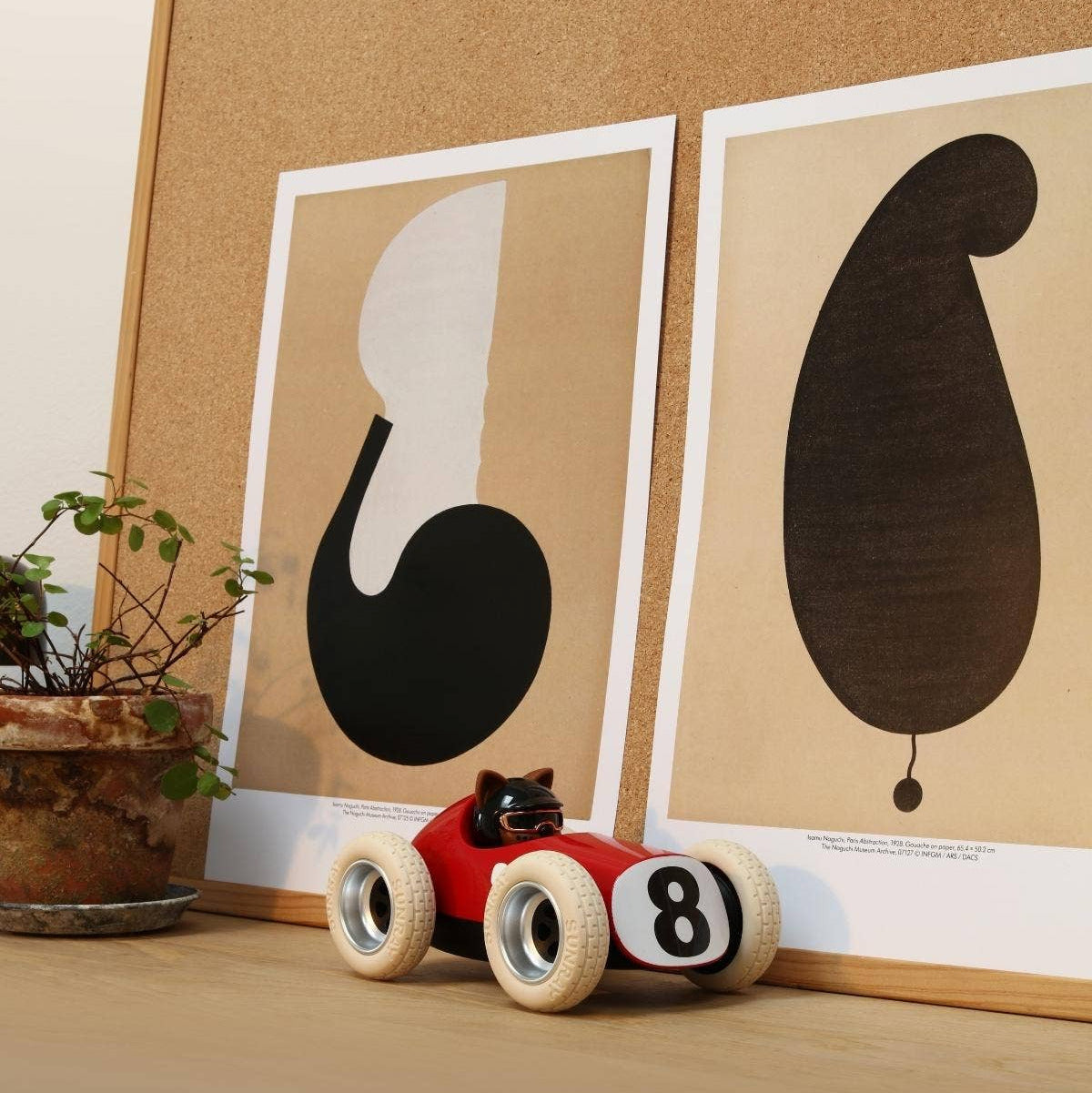 Red toy car with number 8 on a wooden surface in front of framed abstract art.
