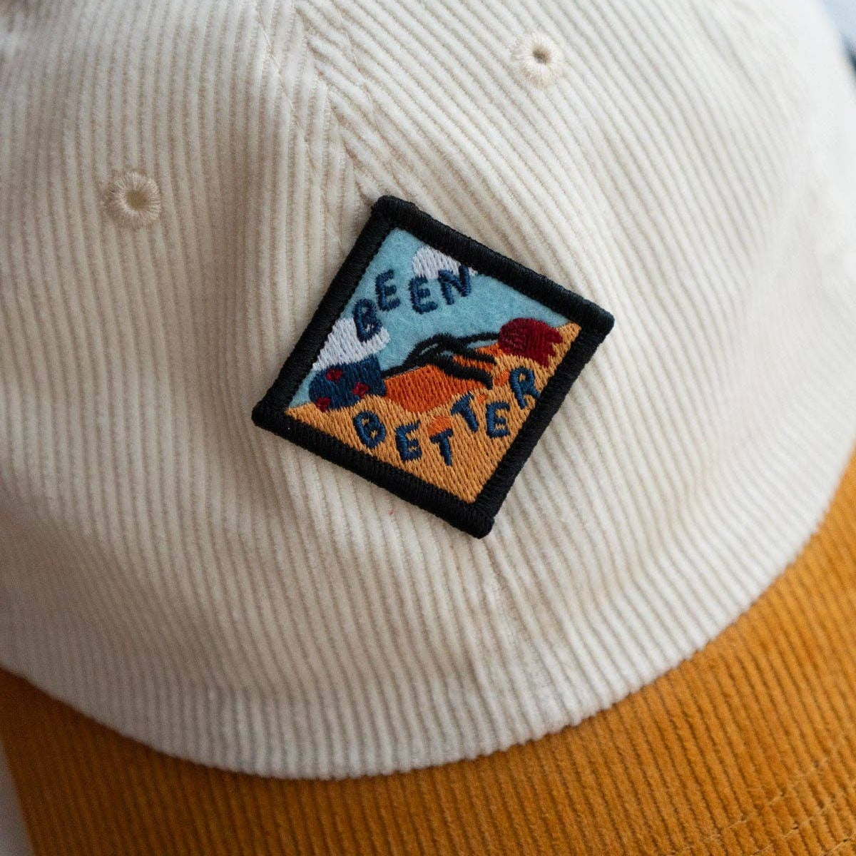 Beige and brown cap with a patch that says 'Been Better' on a light blue background