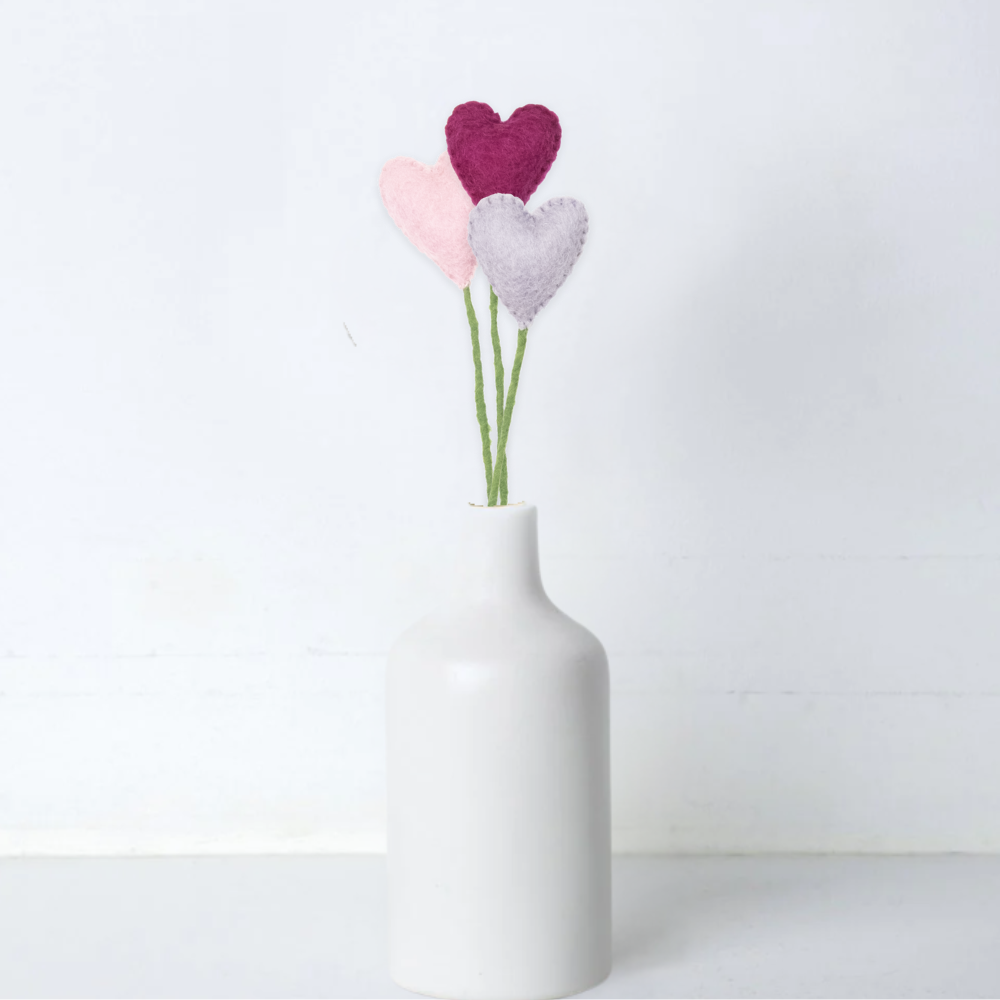 White vase with three felt heart flowers on a white background
