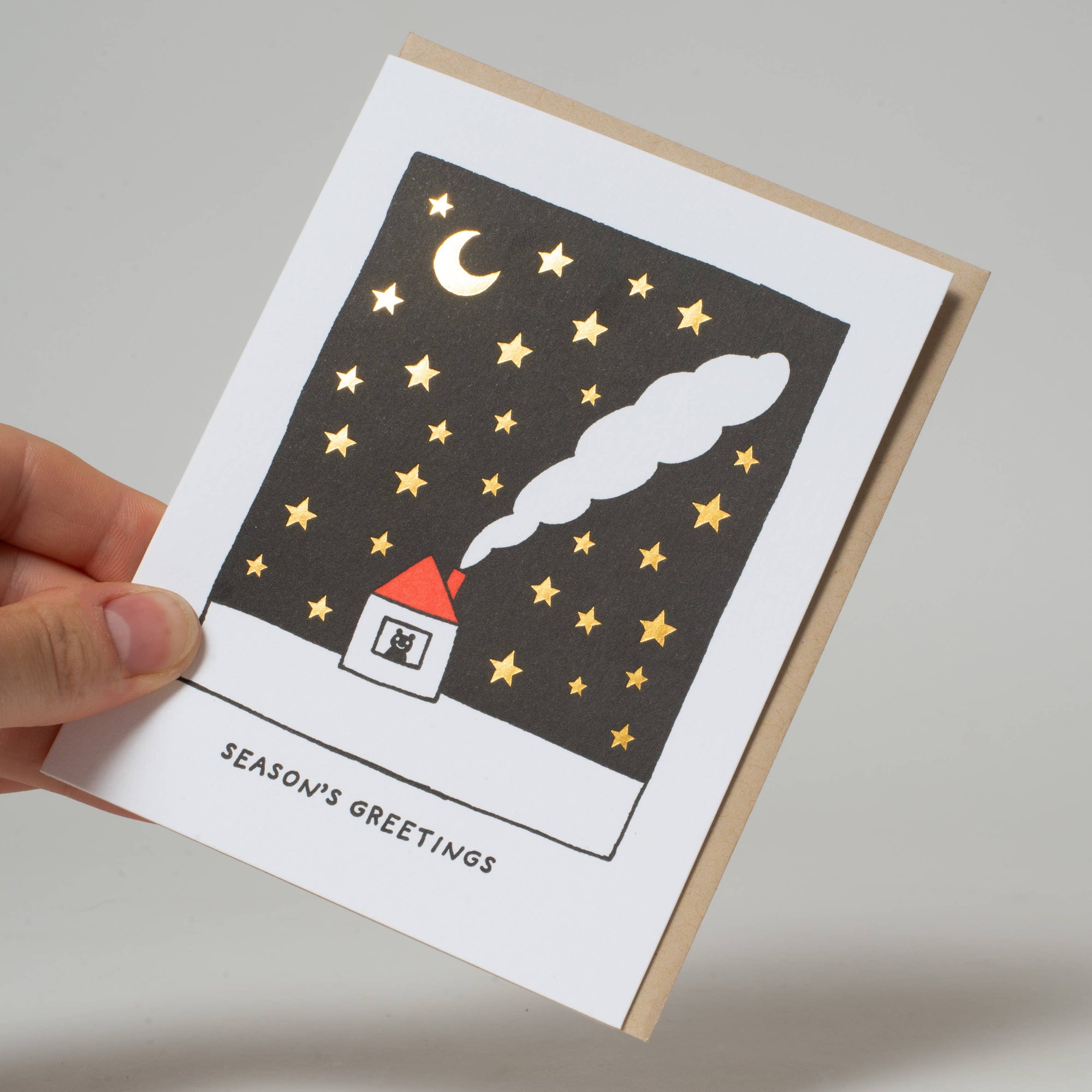 Greeting card with a house, moon, and stars design held by a hand on a neutral background