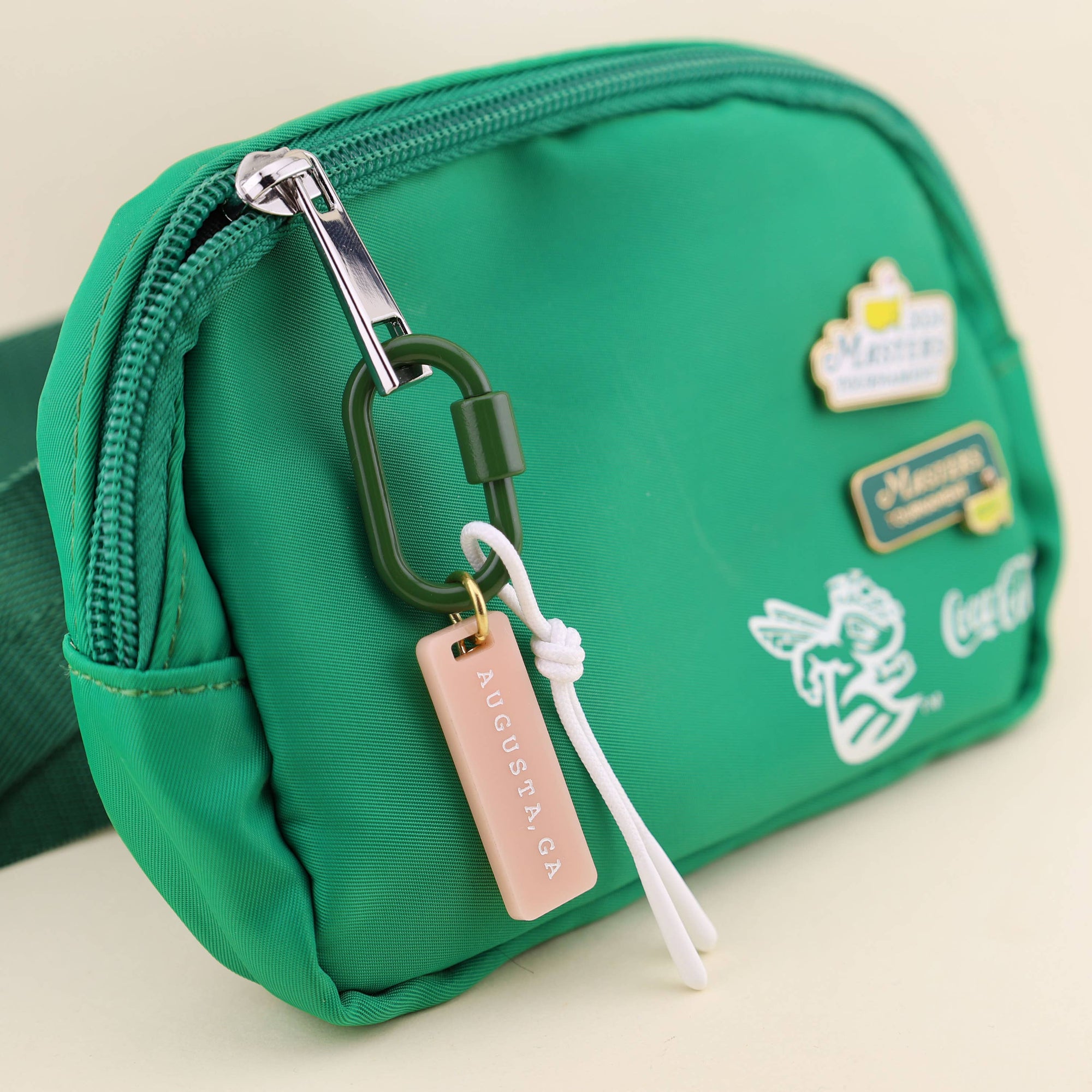 Green waist bag with multiple tags and a keychain on a beige background