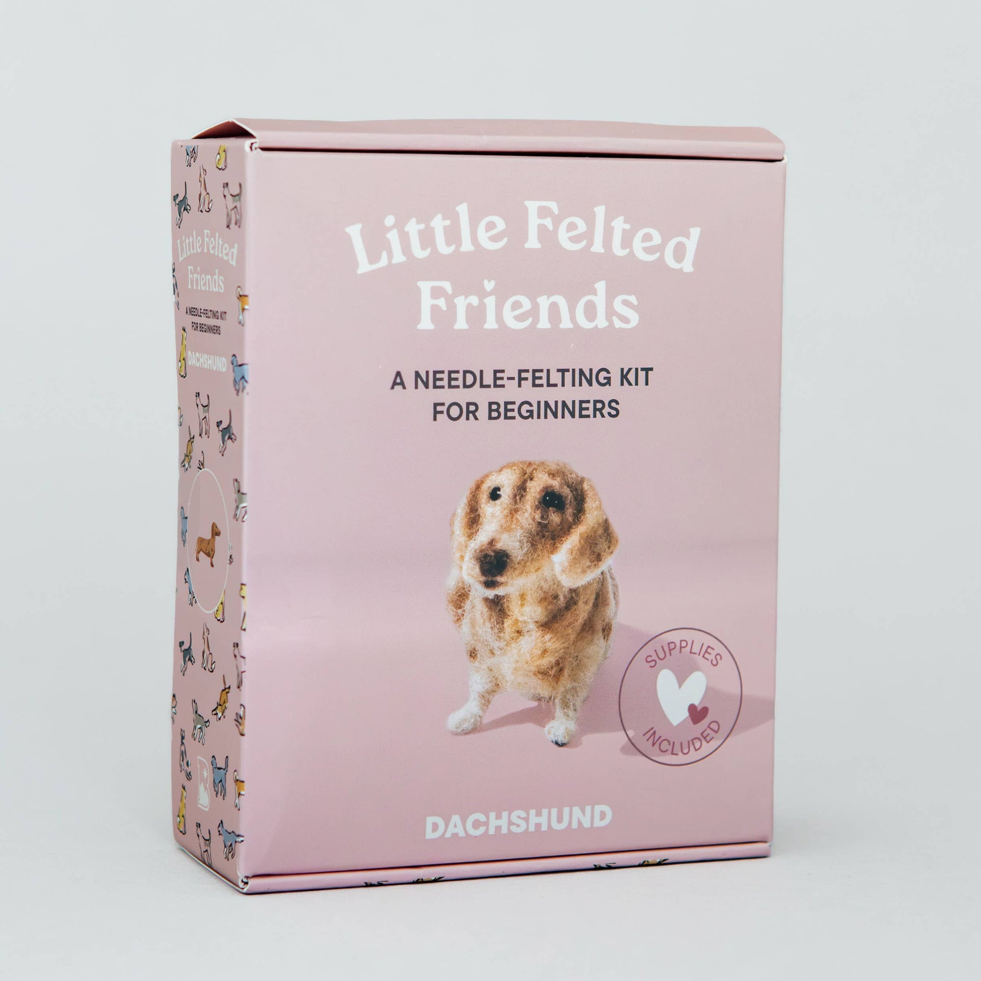A pink box for a needle-felting kit titled 'Little Felted Friends' with a Dachshund pictured on the front, photographed against a light gray studio background.