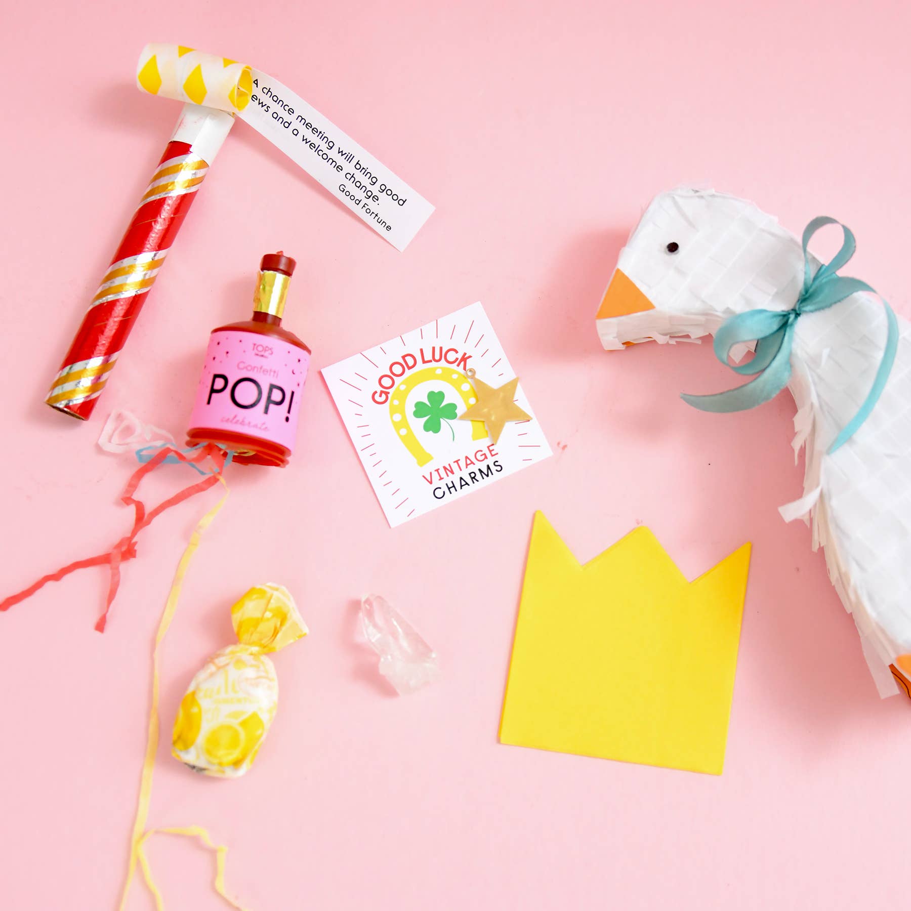 Assorted party favors including a noisemaker, bottle labeled 'POP!', card, and toy on a pink background