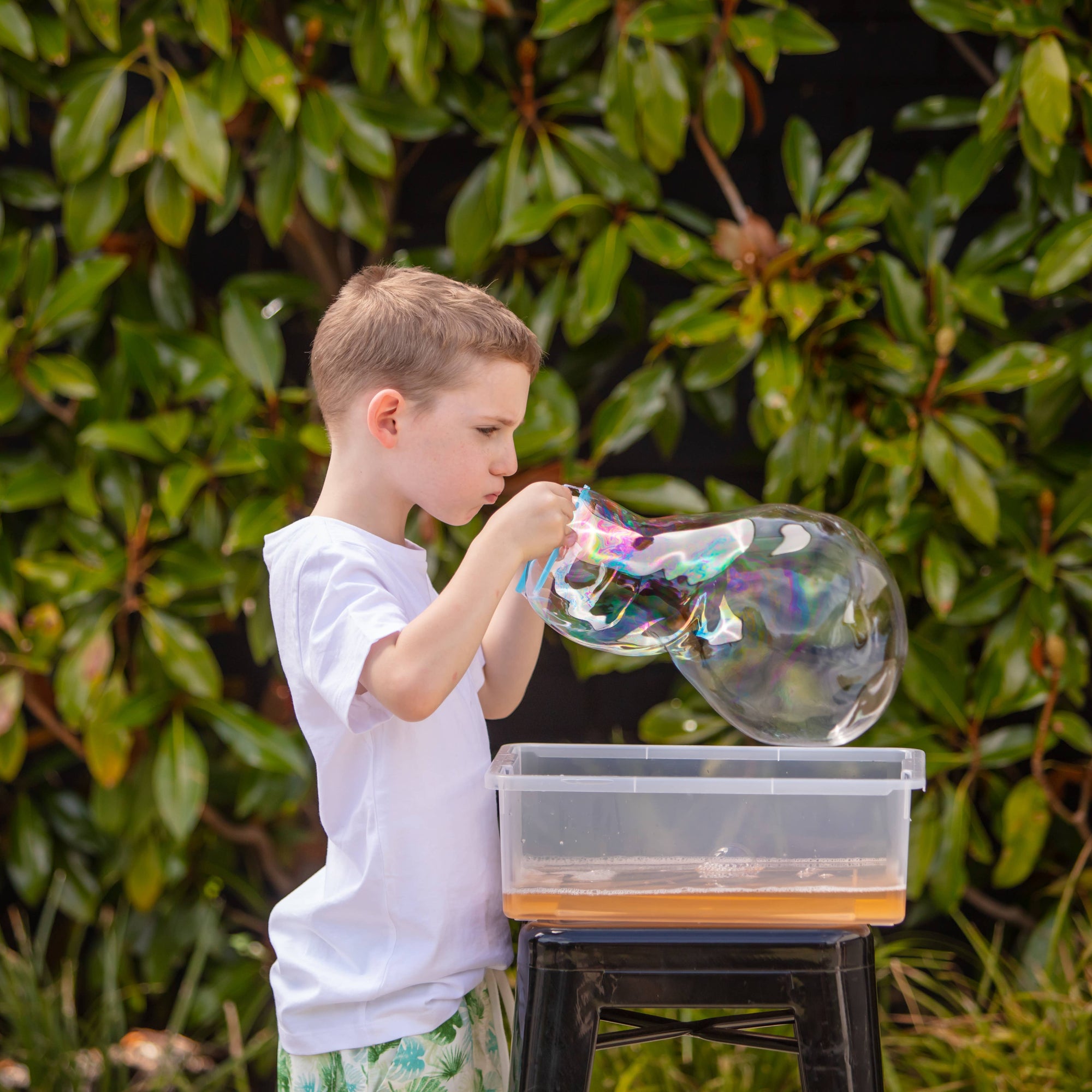 Child blowing bubbles outdoors with a green leafy background