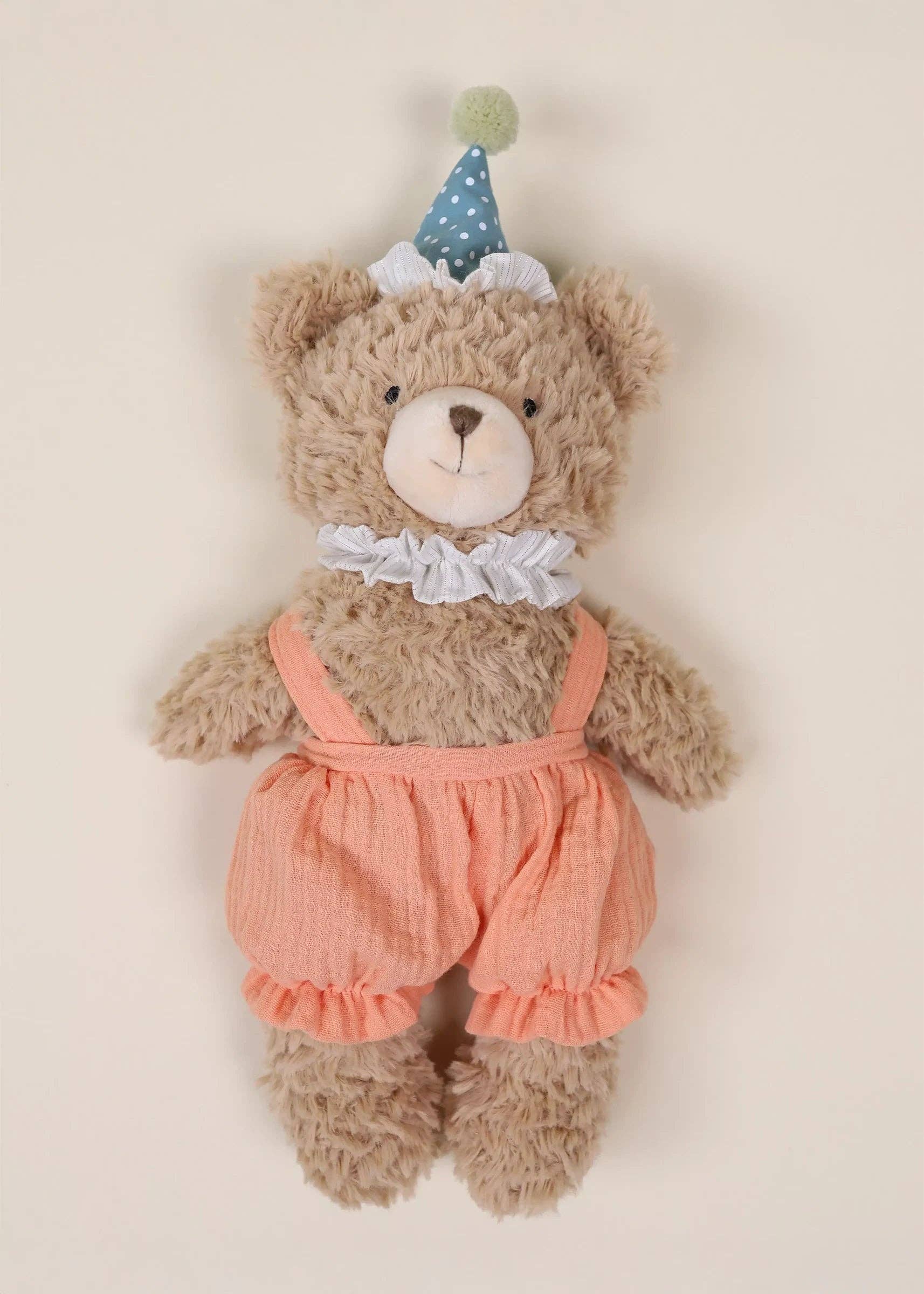 Teddy bear wearing a peach romper and party hat on a beige background