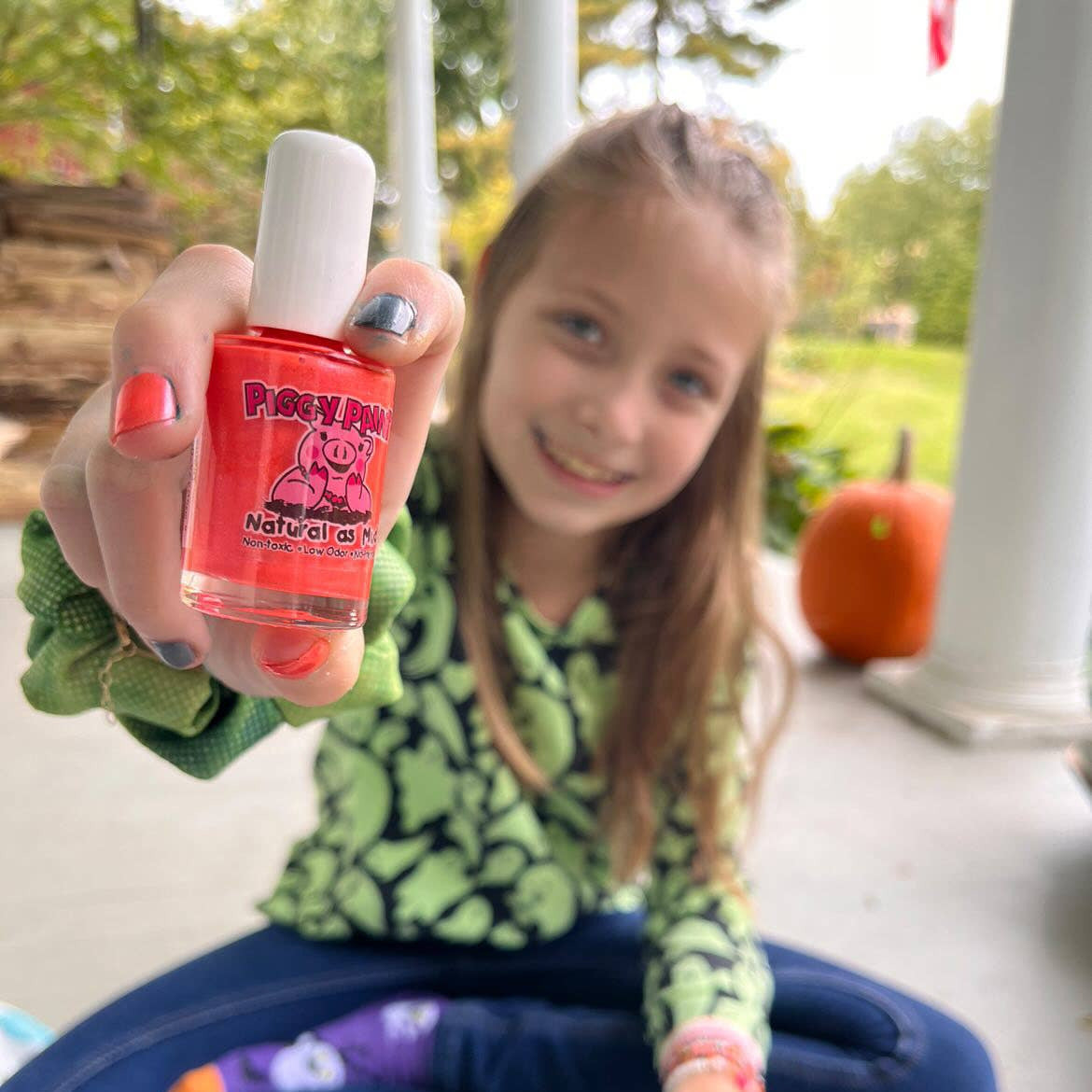 Young girl holding a bottle of pink nail polish on a porch with a pumpkin in the background