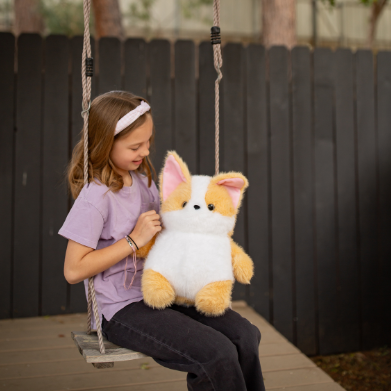 Child sitting on a swing with a plush toy, surrounded by trees and a fence.