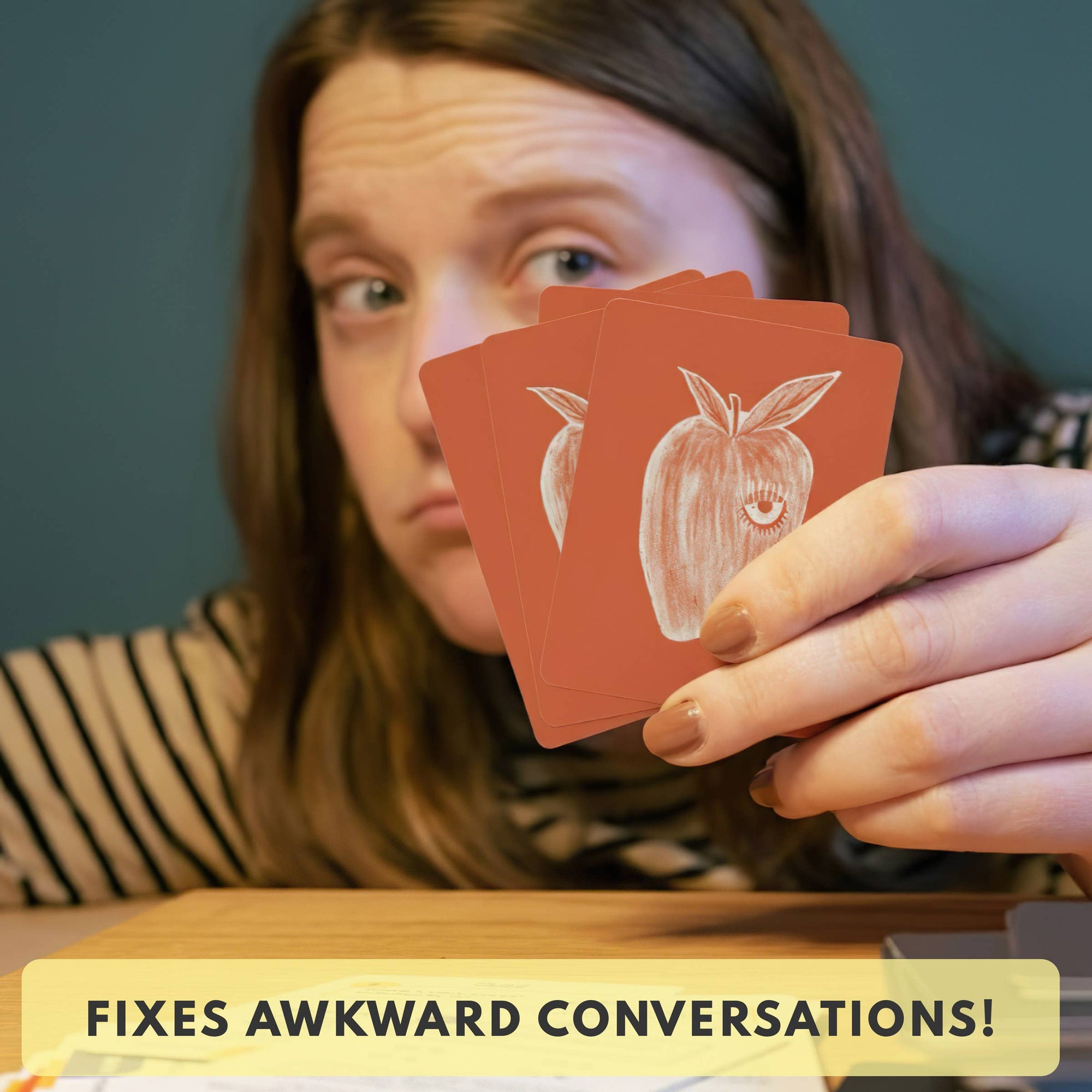 Person holding playing cards with an apple symbol, text 'FIXES AWKWARD CONVERSATIONS!' at the bottom.