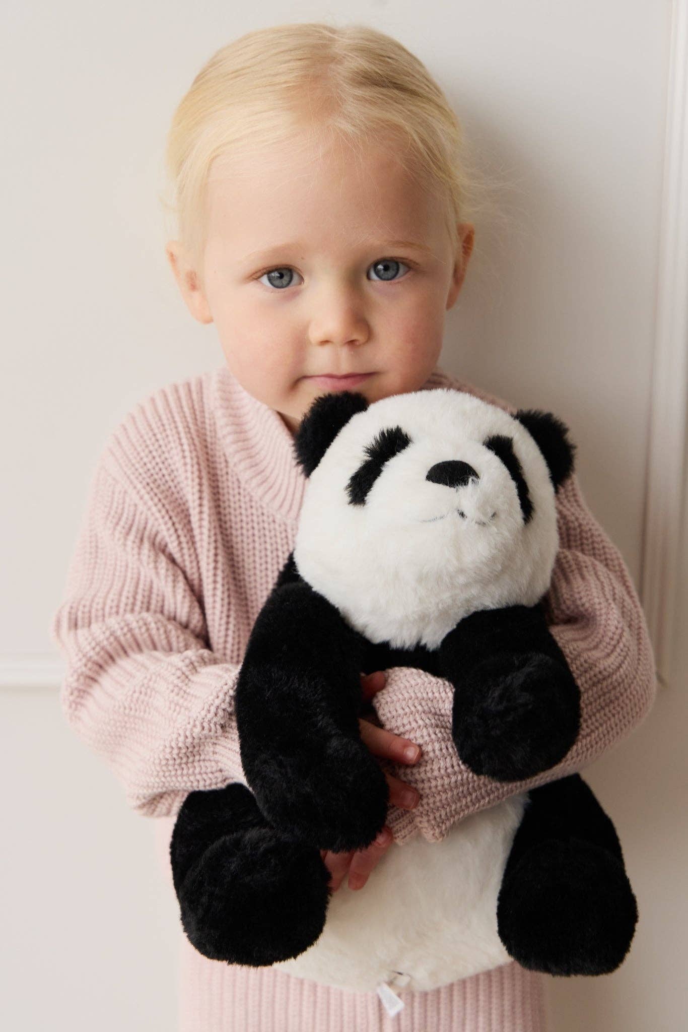 Child holding a panda plush toy against a plain background