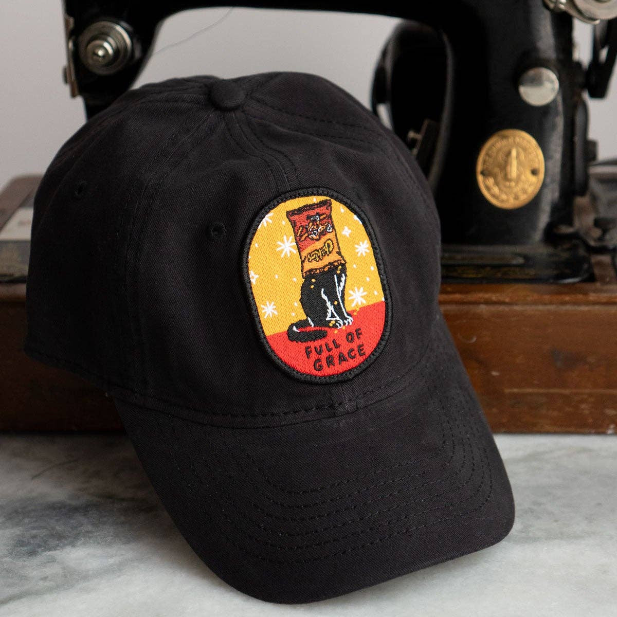 Black cap with a patch in front of an old Singer sewing machine.