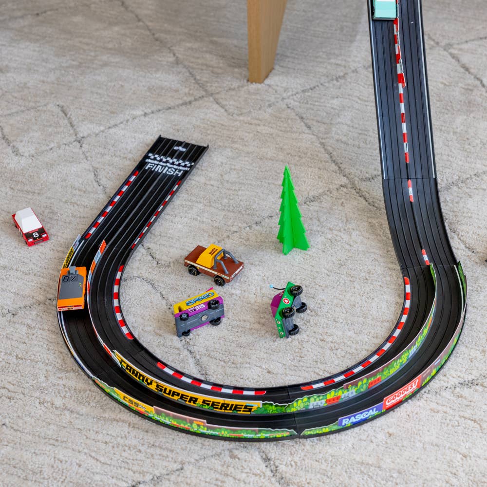 Toy race track set up on a concrete floor with toy cars and a tree.