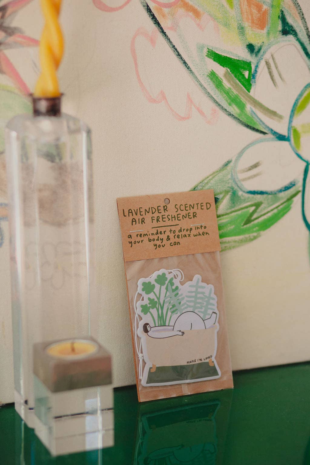 Lavender scented air freshener package with a candle and decorative item in the background.