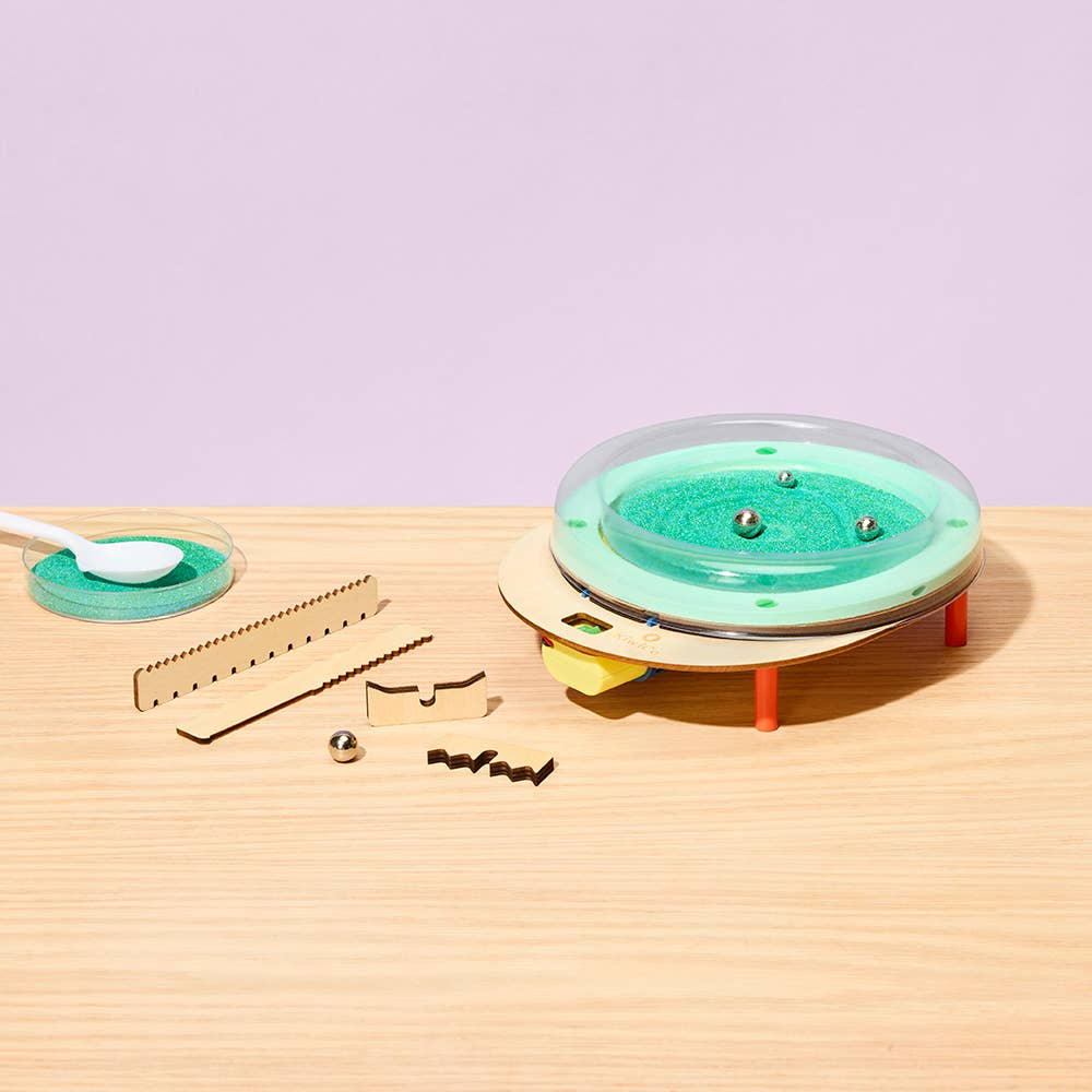 Toy bathtub with green water, toy bathtub tools, and a spoon on a wooden surface with a light purple background.
