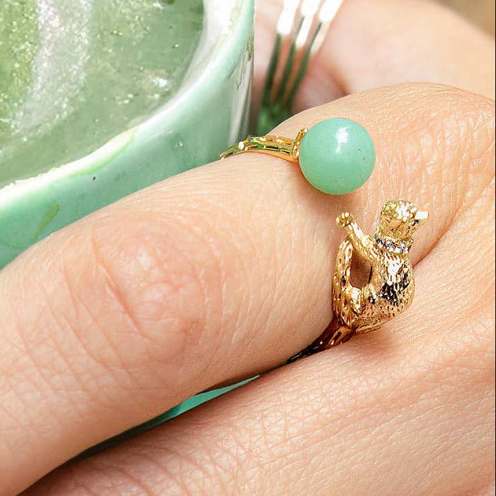 Green latte in a cup with a hand wearing gold rings on a wooden surface