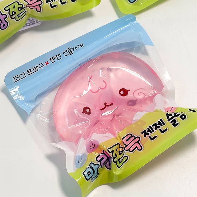 A pink cartoonish squishy toy inside a clear plastic bag with a blue header and yellow-green Korean text label, photographed on a white surface.