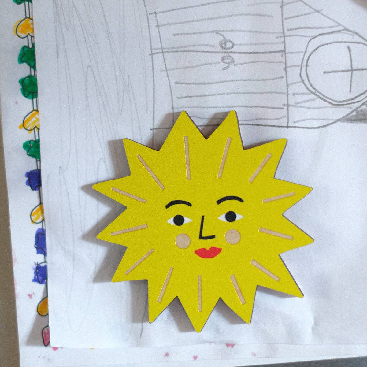 Yellow sun-shaped object with a face on a piece of paper with drawings.