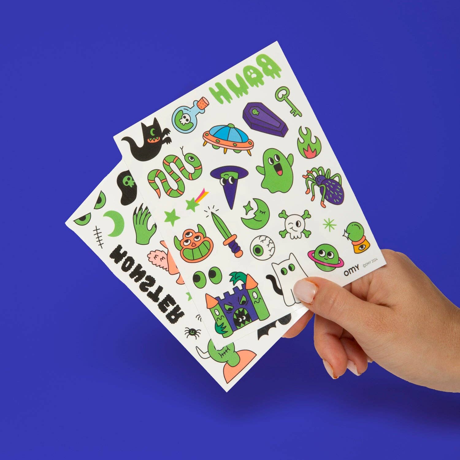Hand holding a sheet of colorful Halloween-themed stickers against a blue background
