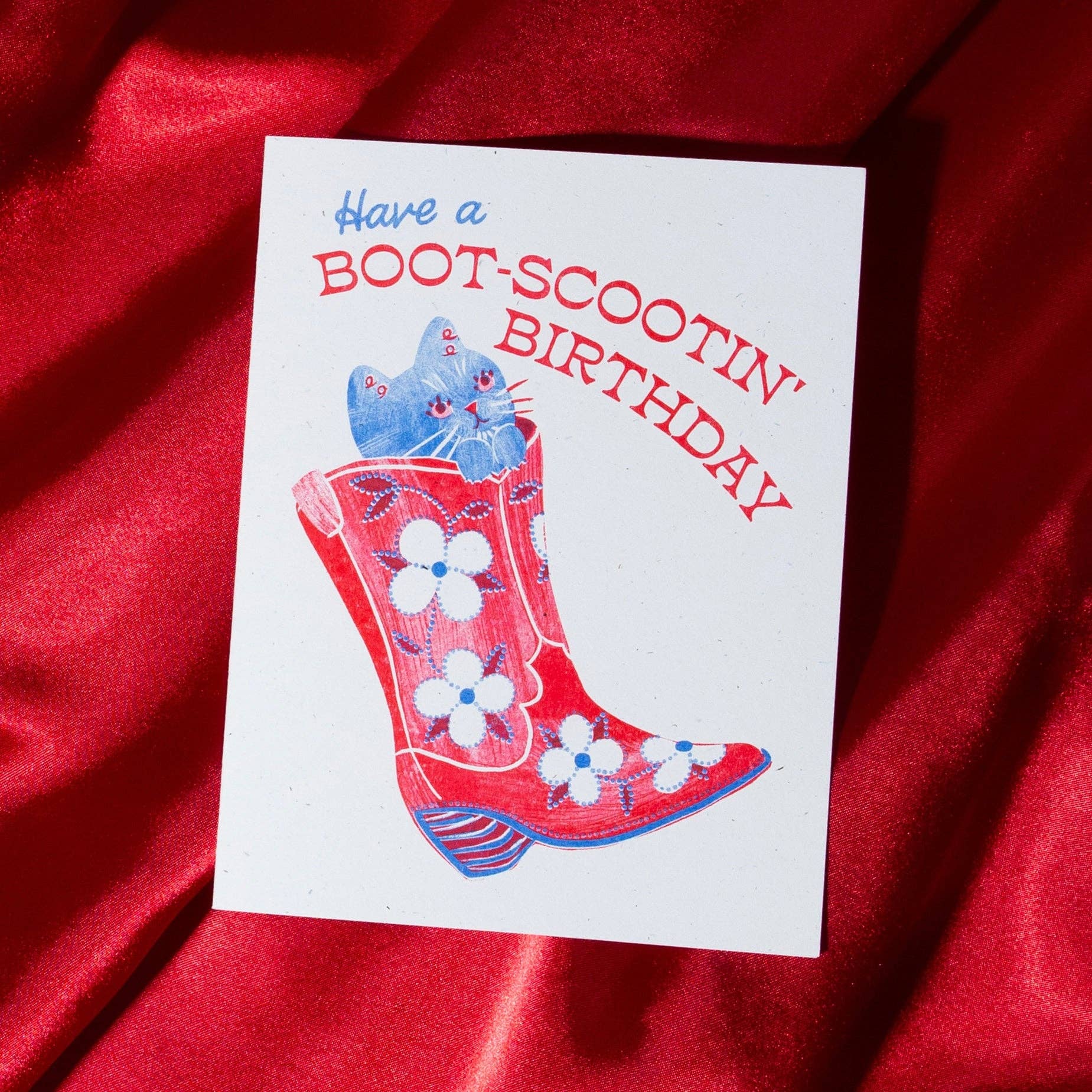 Greeting card with a boot and cat illustration on a red fabric background