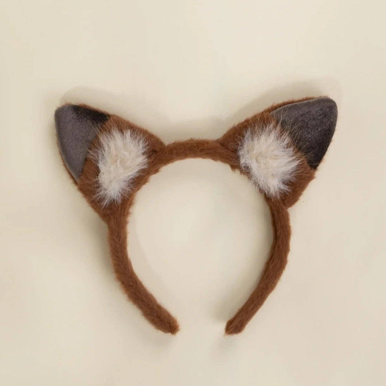 A brown faux-fur animal cat ears headband with dark gray inner ears and white fluffy accents, displayed on a light cream background.