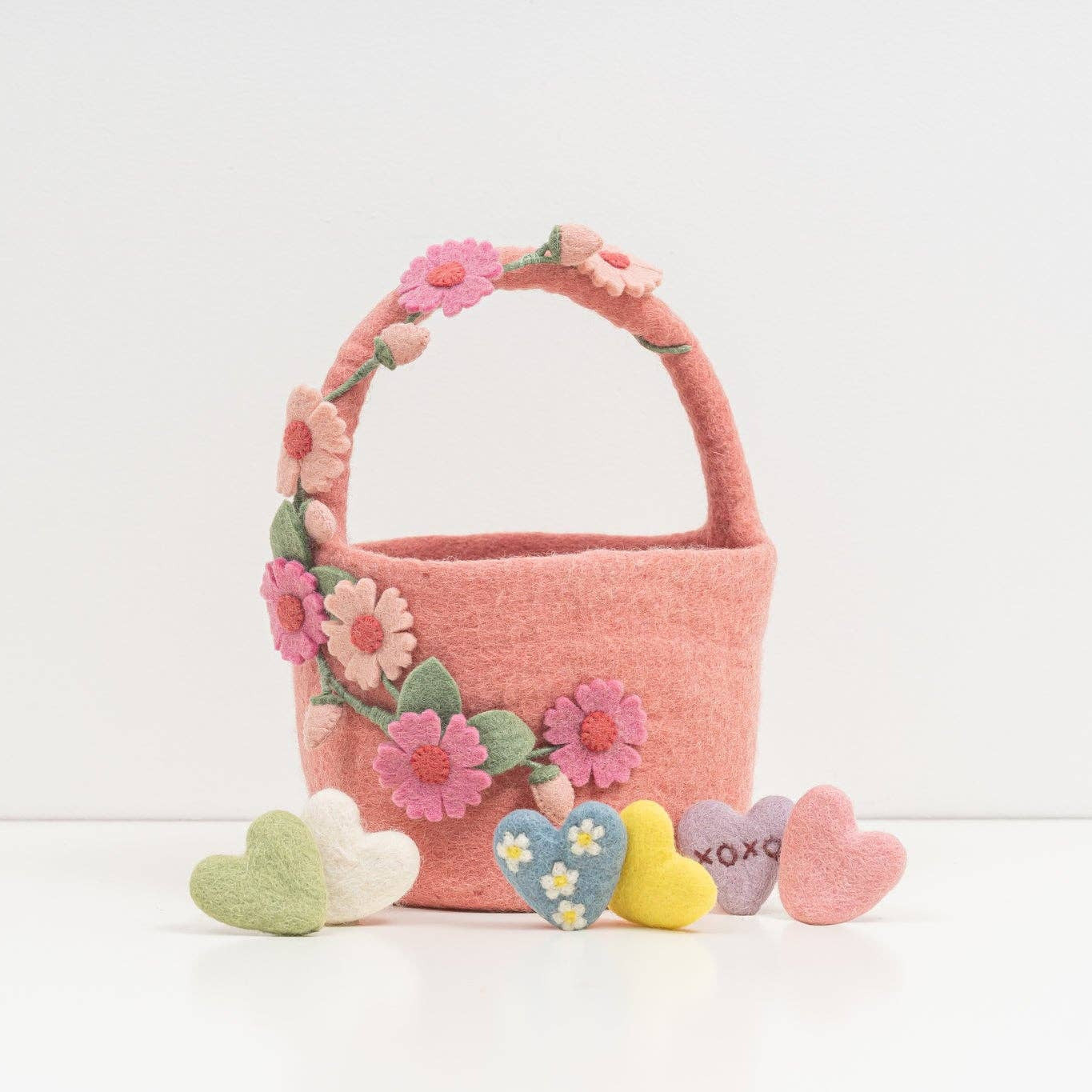 Pink woven basket with floral decorations and heart-shaped tokens on a white background