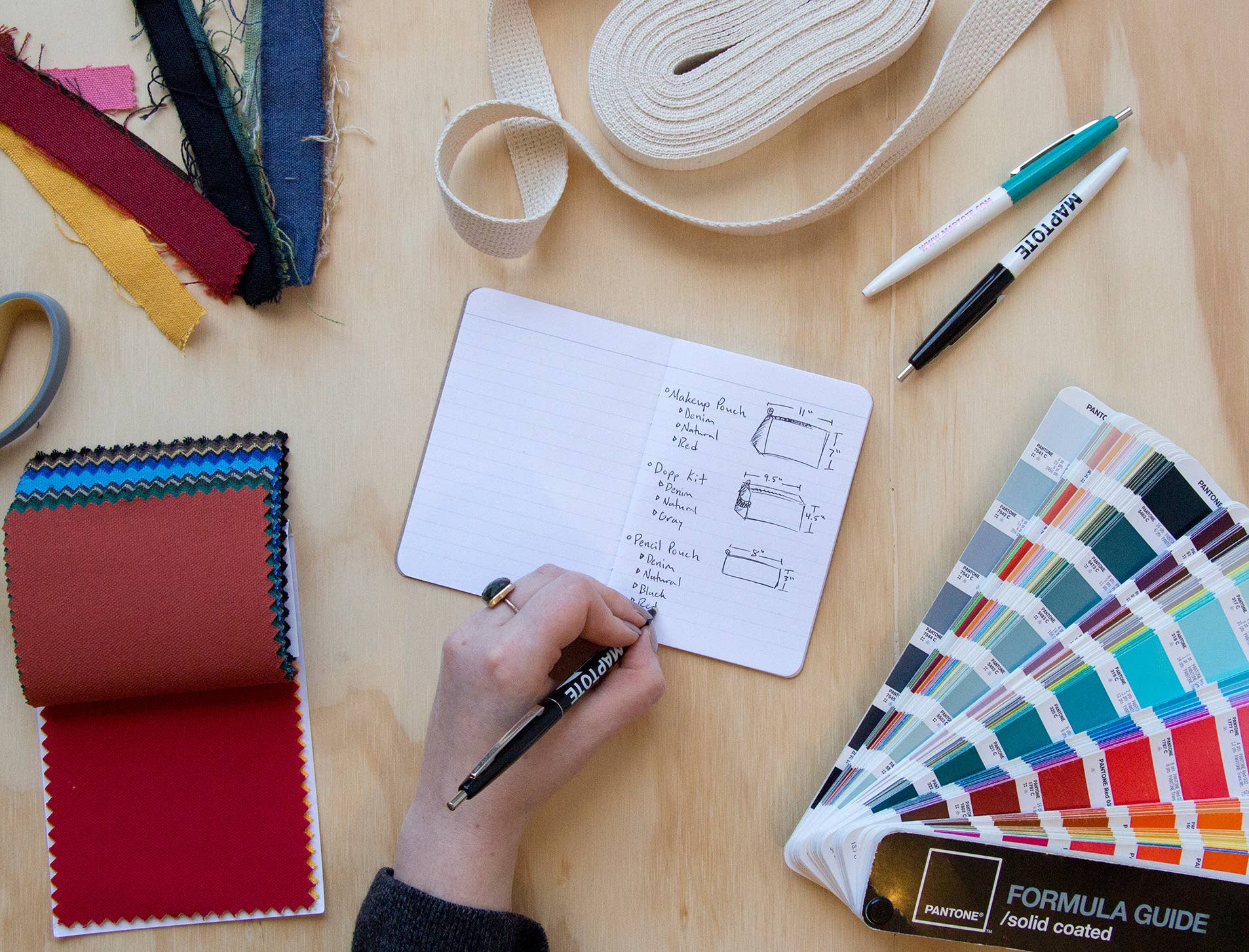 Design process with fabric swatches, color chart, and design tools on a wooden table.