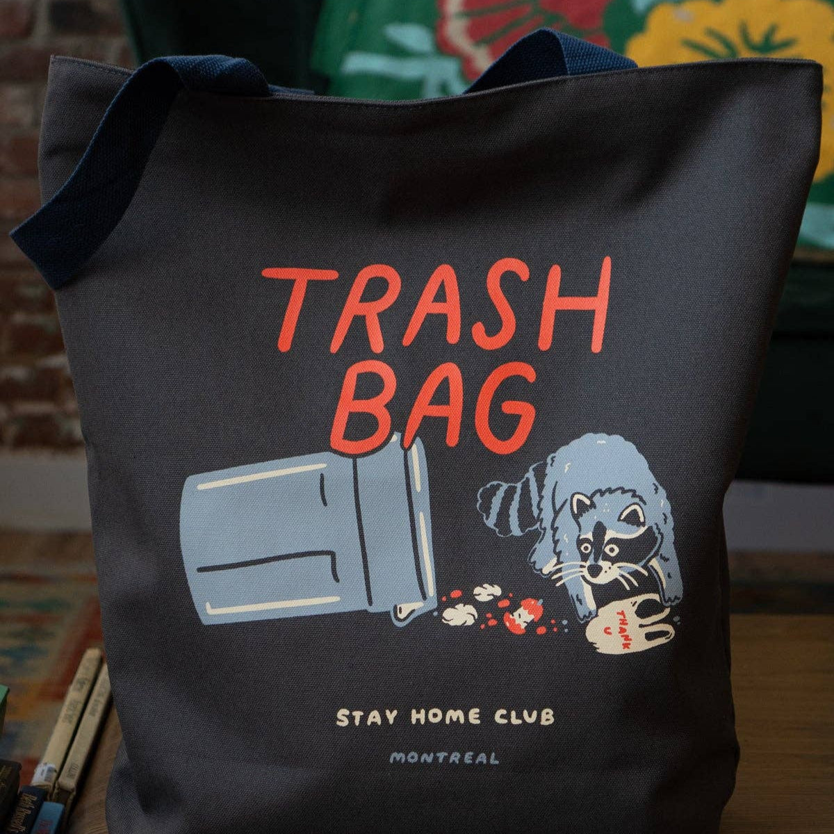 Black tote bag with 'Trash Bag' text and graphic design on a wooden surface.