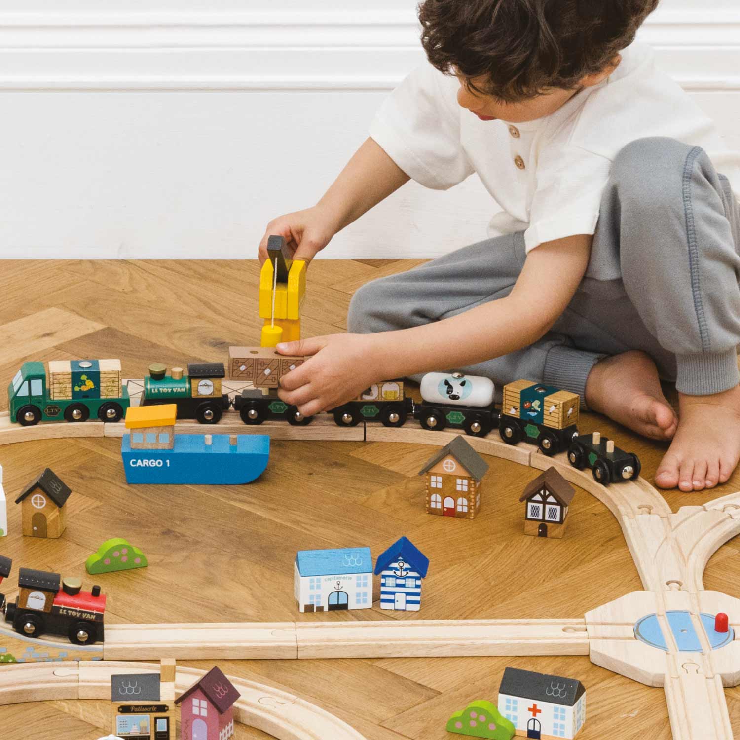 Child playing with a wooden train set on a wooden floor