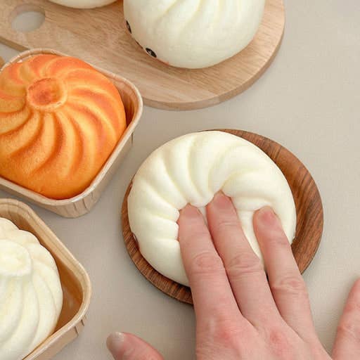 Hand holding a white steamed bun on a wooden plate with other buns in the background.