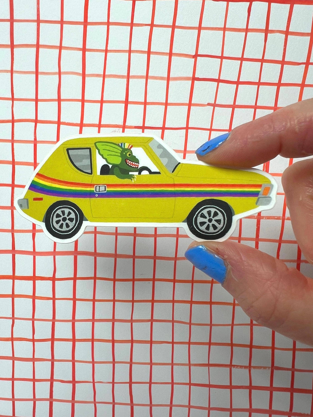 Colorful toy car with a dragon design held by a hand against a grid background