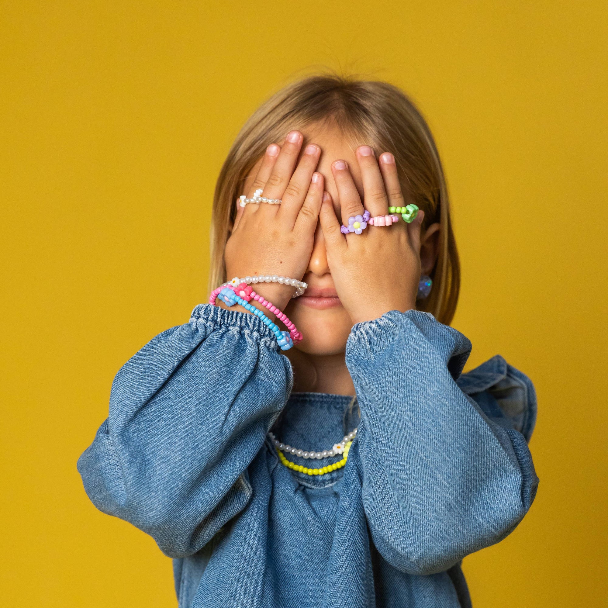 Child wearing a denim shirt with colorful bracelets on a yellow background
