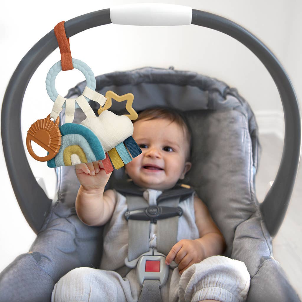 Baby in a car seat with a colorful toy hanging from the headrest