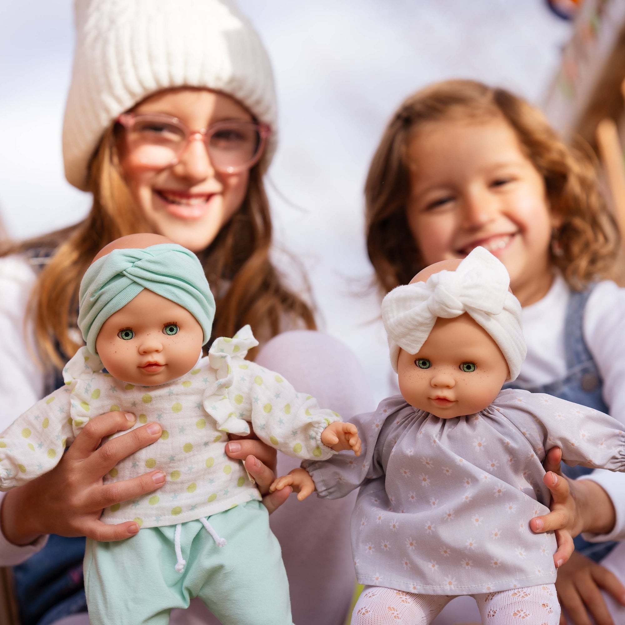Two children holding dolls outdoors, with a wooden structure in the background