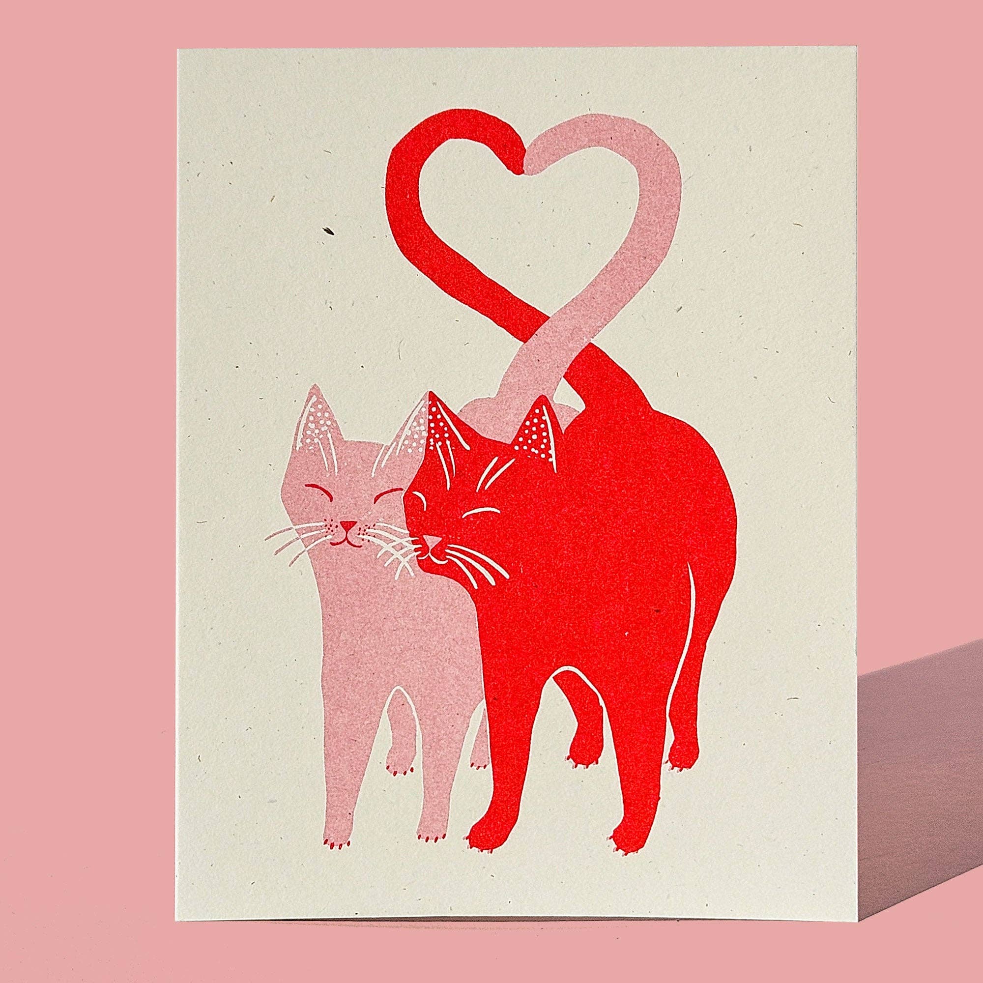 Illustration of two cats forming a heart shape on a beige card with a pink border.