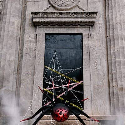 A large black spider decoration with red details and white web strands hanging in front of a stone building doorway.