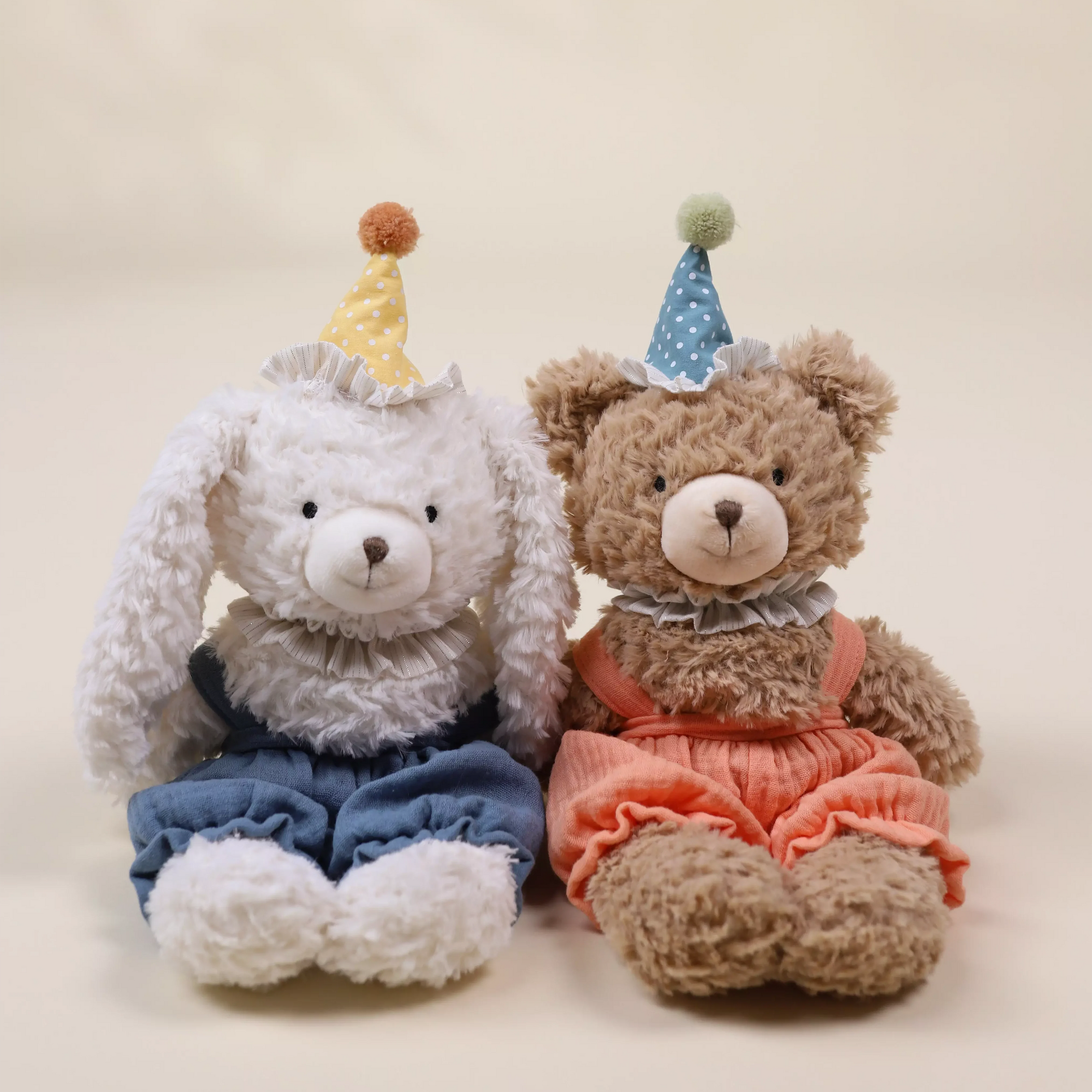 Two teddy bears, one gray and one brown, wearing party hats and outfits on a beige background.