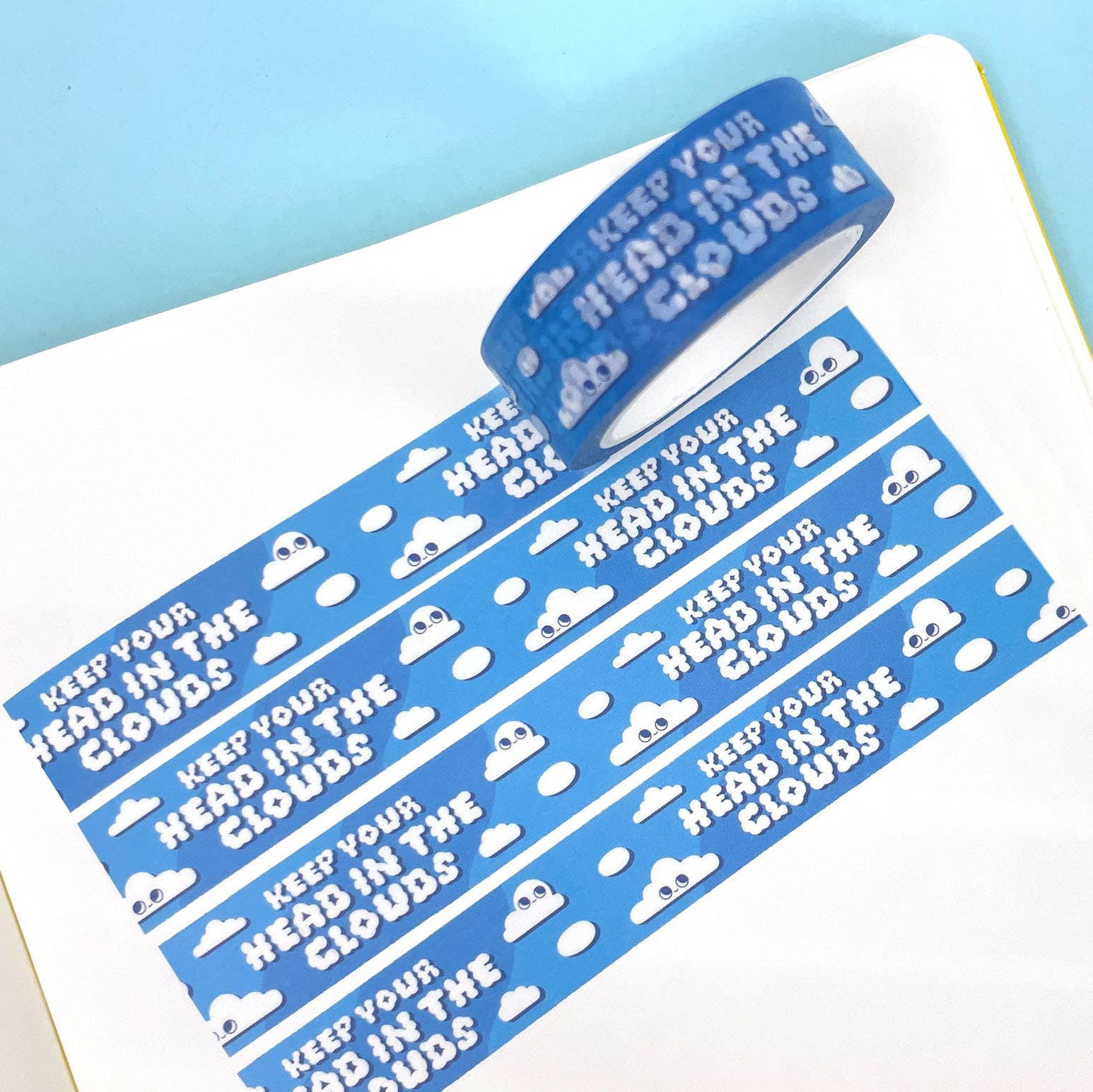 Roll of blue washi tape with 'Keep your head in the clouds' text on a white surface.