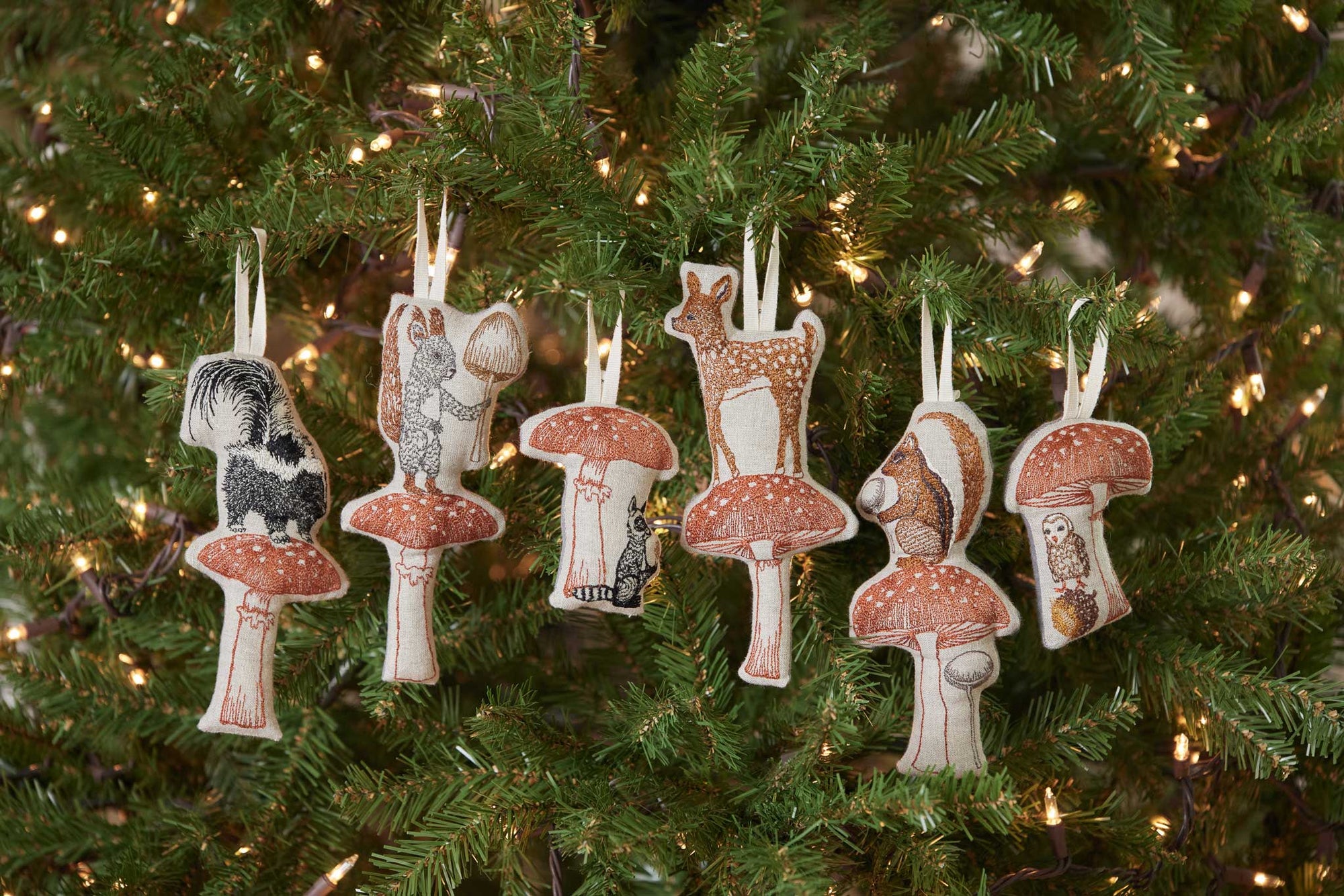 Decorative Christmas ornaments shaped like animals and mushrooms hanging on a tree.