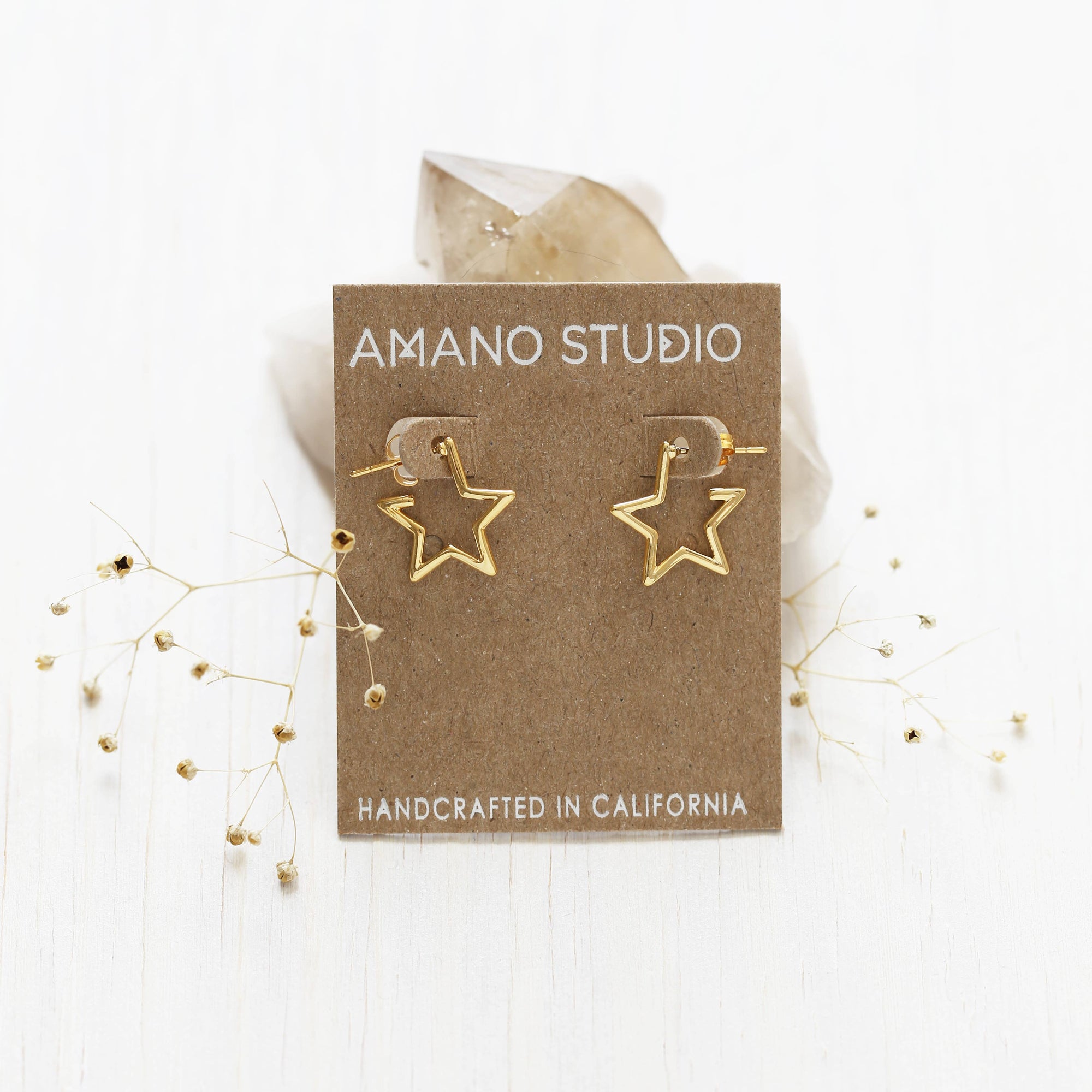 Gold star-shaped earrings on a 'Amano Studio' branded card with a white background