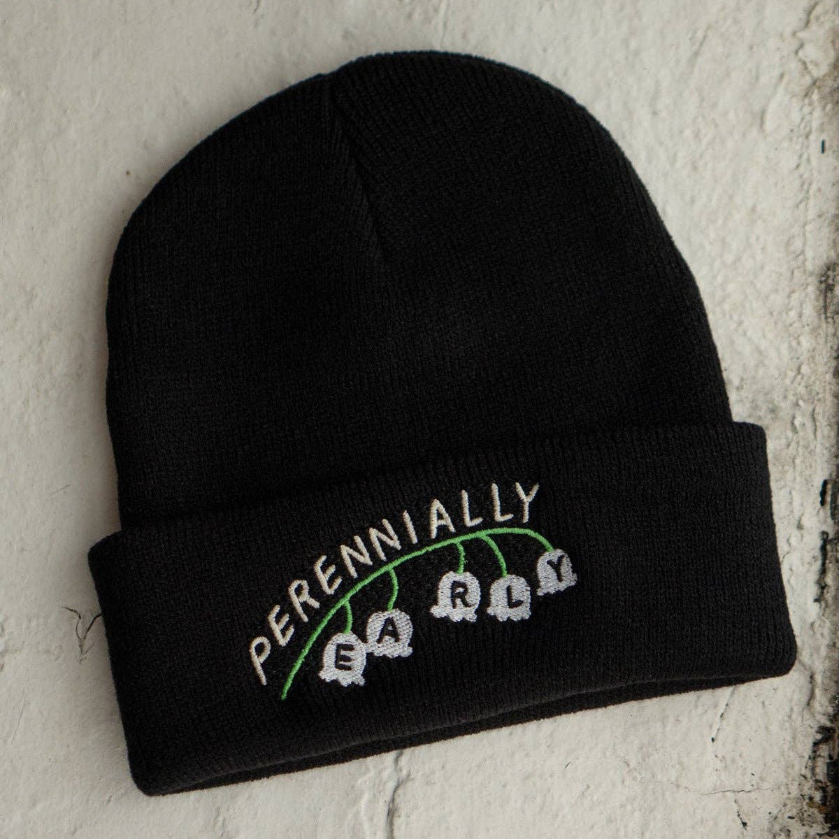 Black beanie with embroidered text on a textured white background