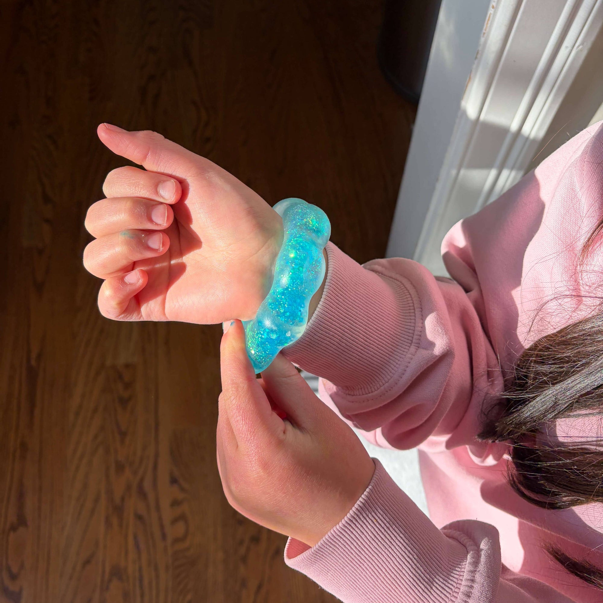 Child wearing a pink sweatshirt and blue glittery bracelet indoors.
