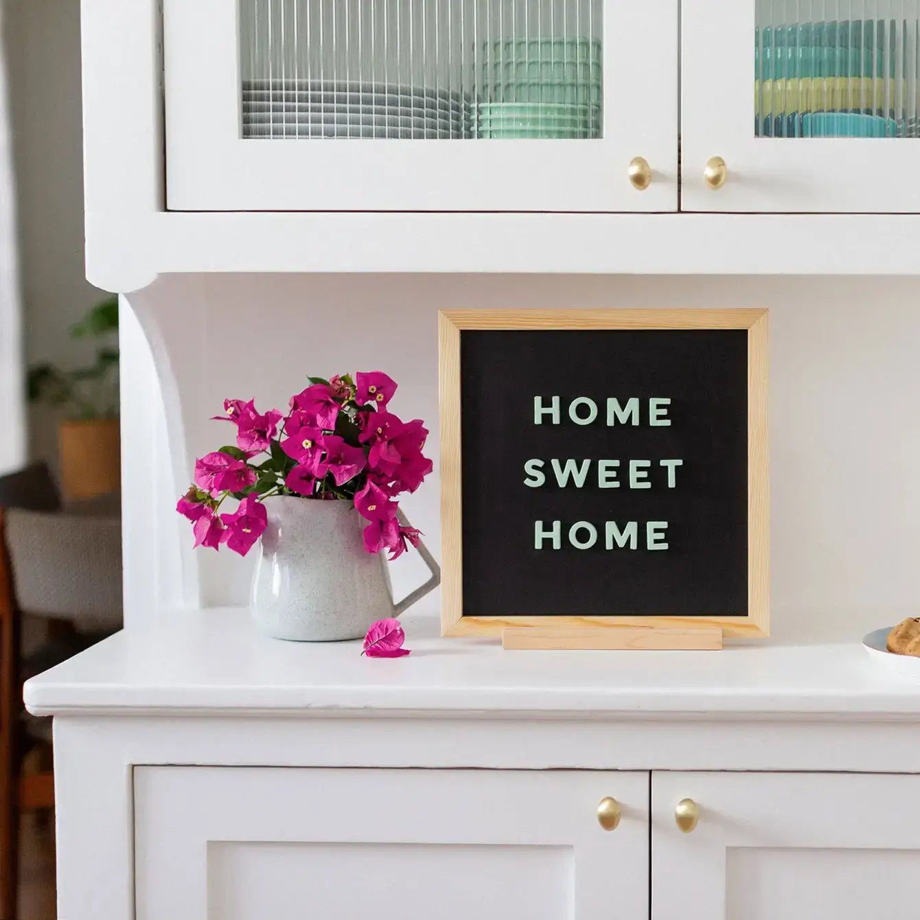 White cabinet with 'Home Sweet Home' sign and pink flowers on a countertop