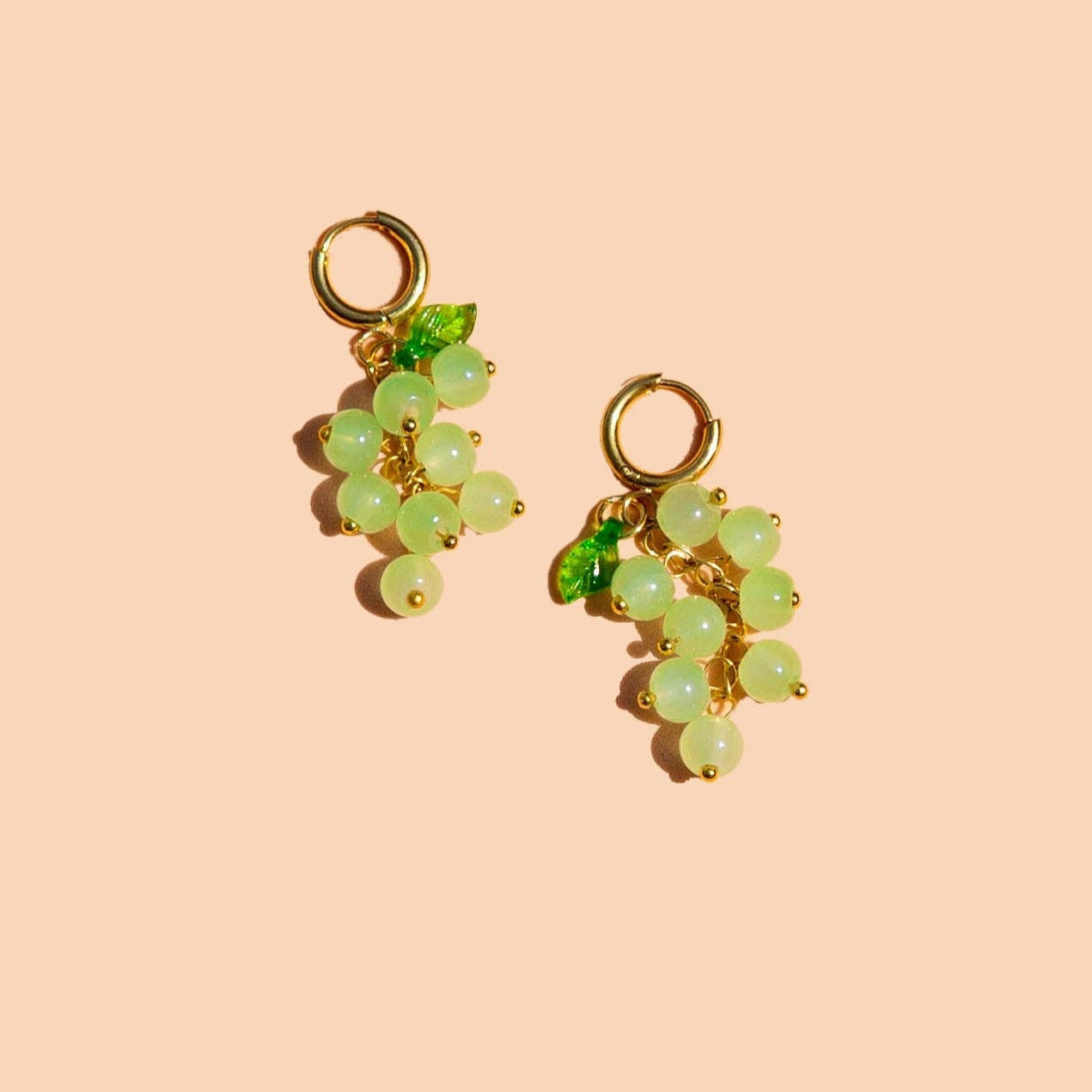 Pair of green grape-shaped earrings on a beige background