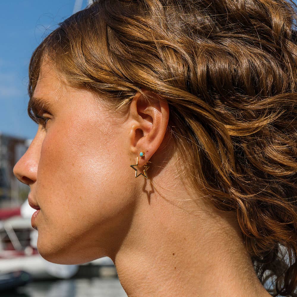 Close-up of a person wearing a gold star-shaped earring with a blue gemstone.