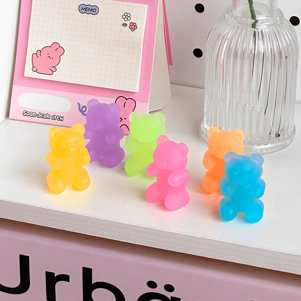 Colorful gummy bear-shaped erasers on a shelf with a pink memo pad in the background.