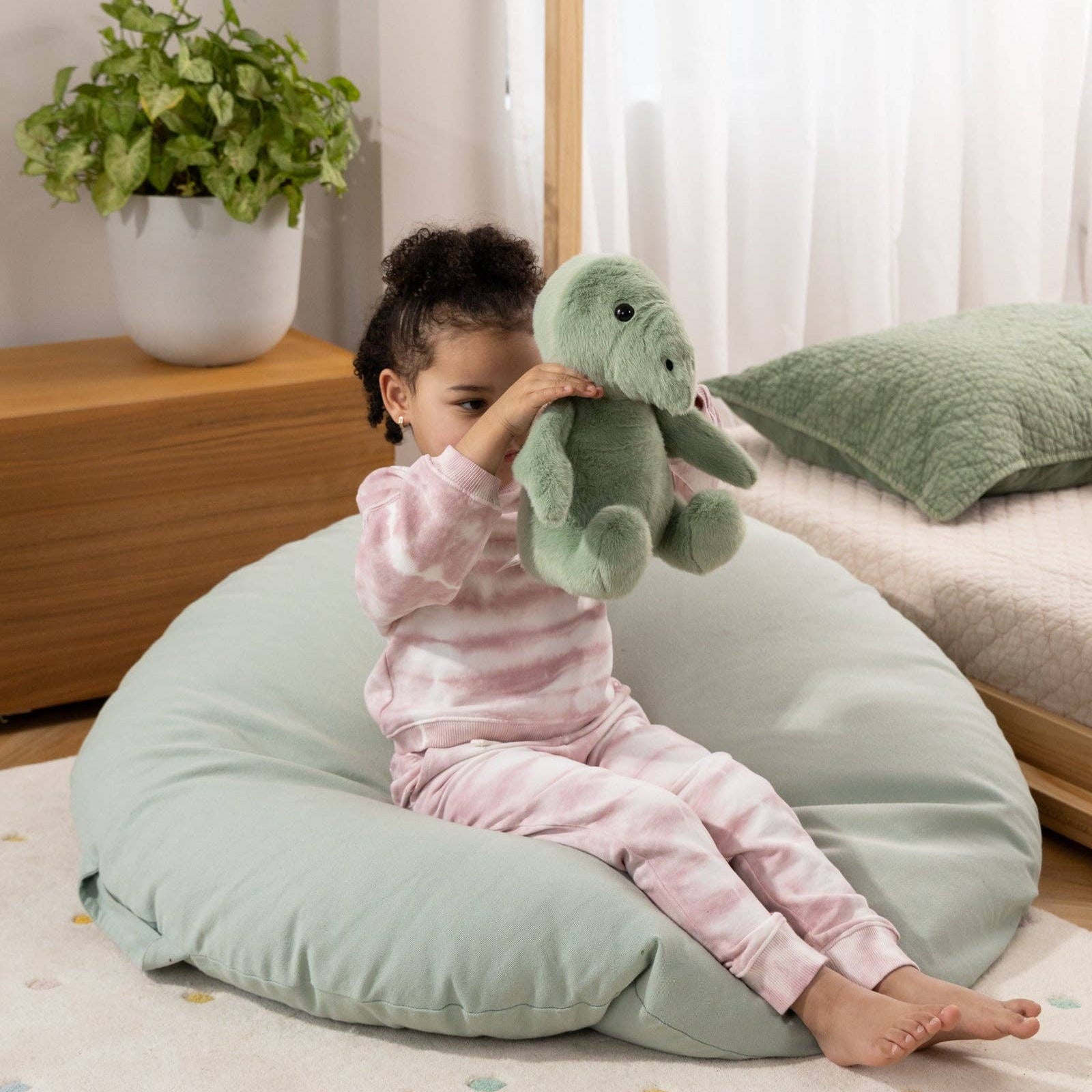 Child sitting on a bean bag holding a plush toy in a cozy room.