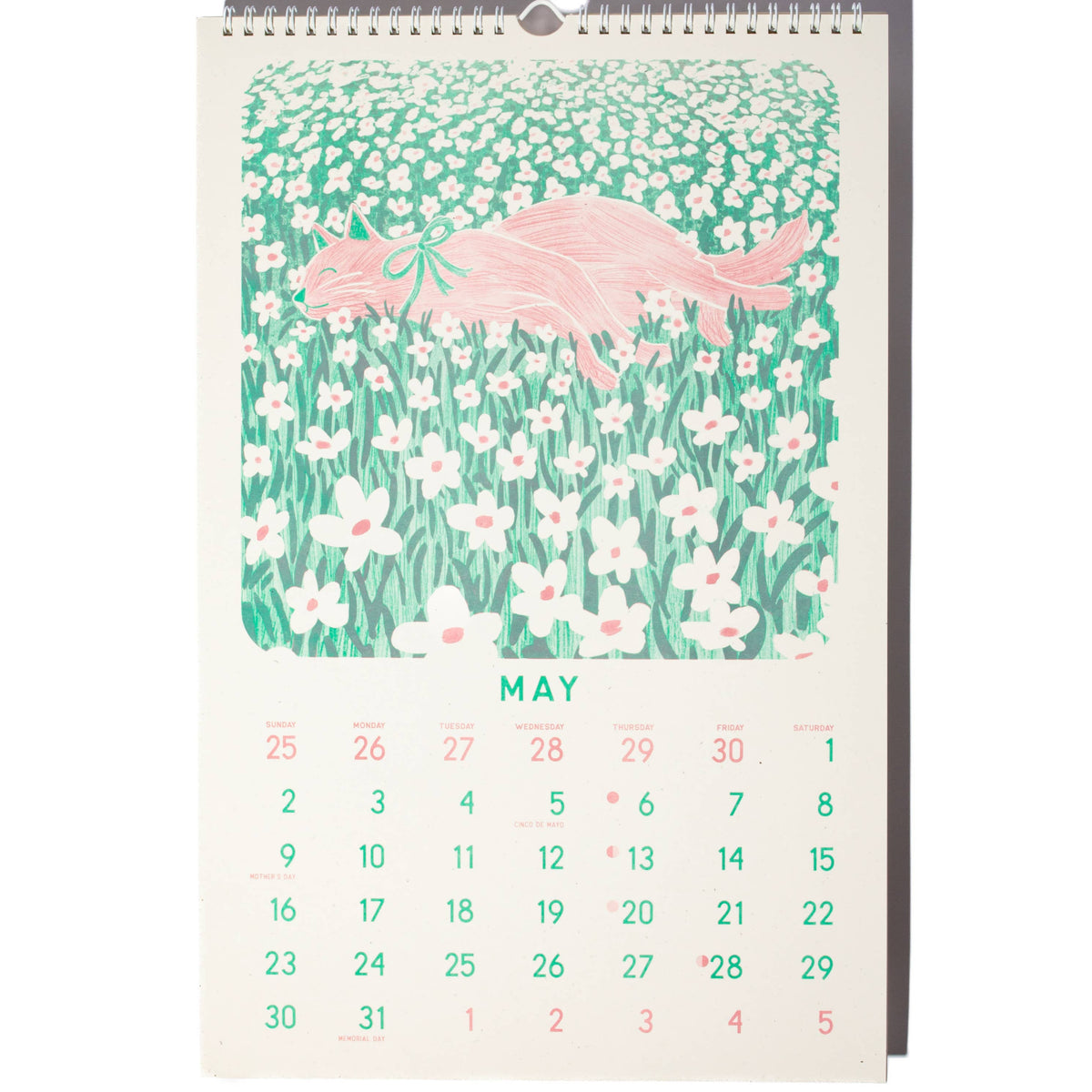 A spiral-bound monthly calendar page showing May, with a pastel illustration of a pink flamingo over a green field of white flowers. The days of the week are printed in green and pink on an off-white background.