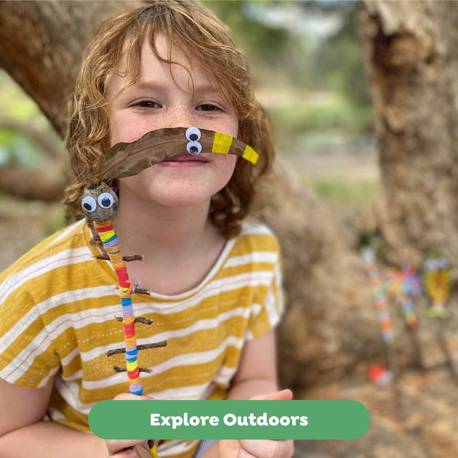 Child holding a stick insect craft with a blurred outdoor background