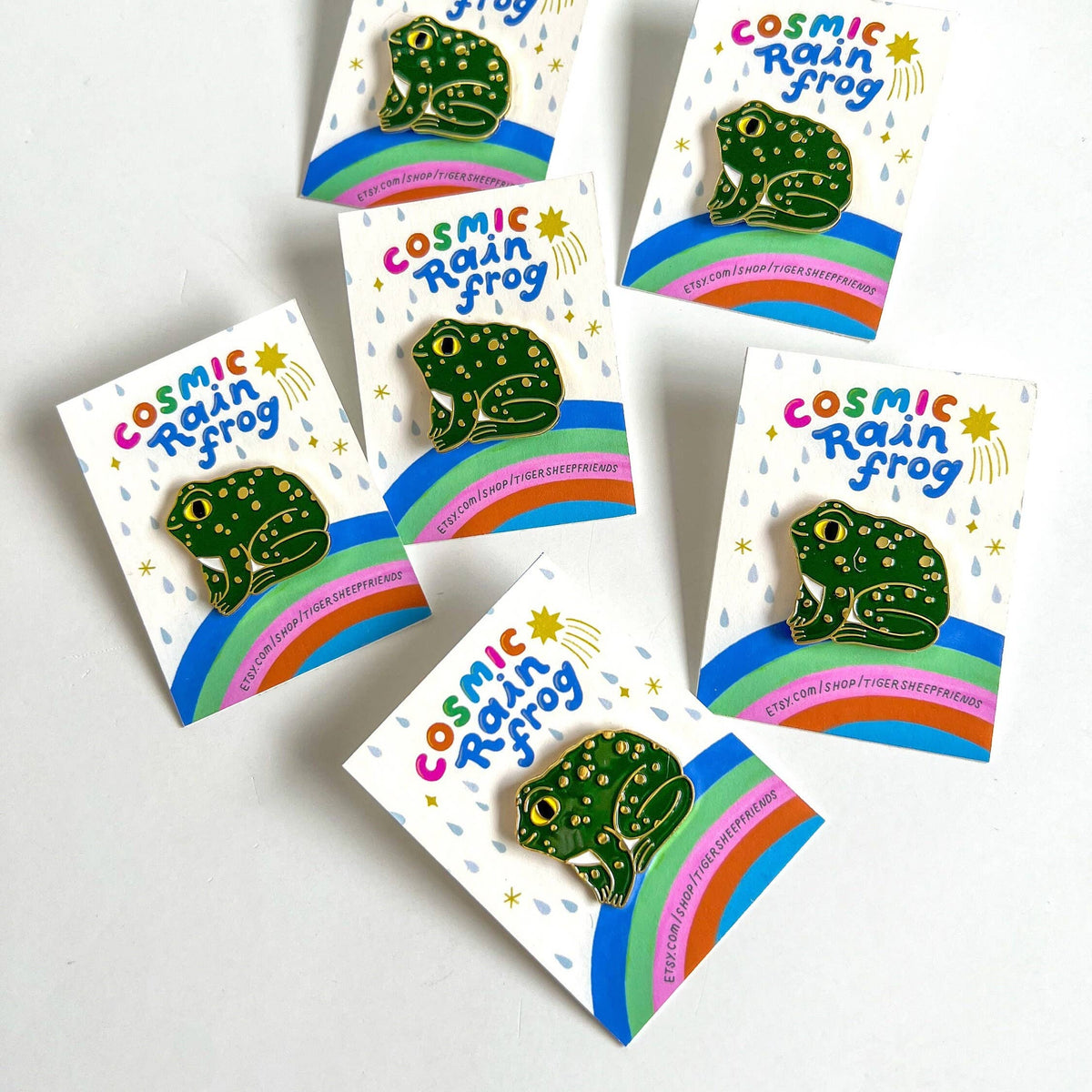 Cosmic Rain Frog pins on white cards with colorful designs