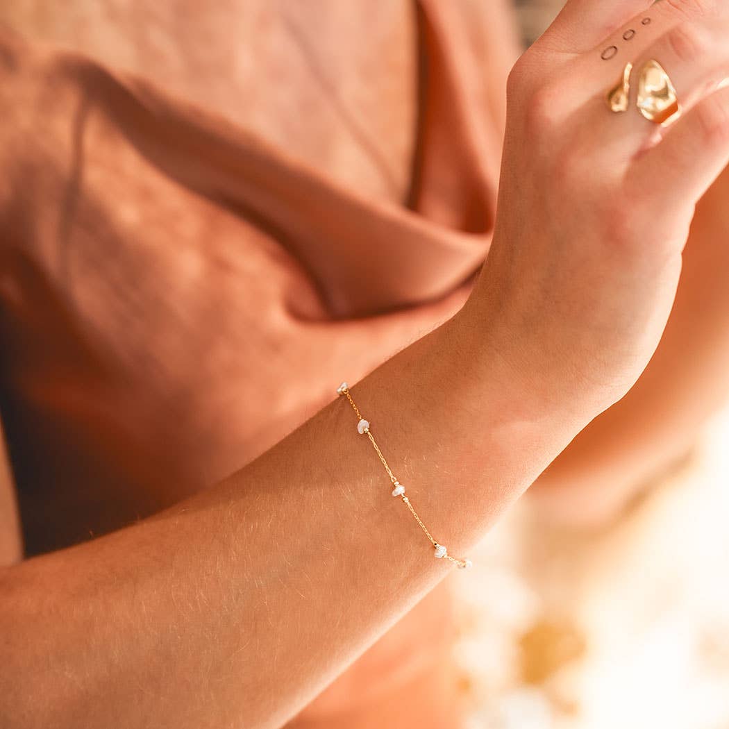 Close-up of a hand wearing a gold bracelet with a soft, blurred background.